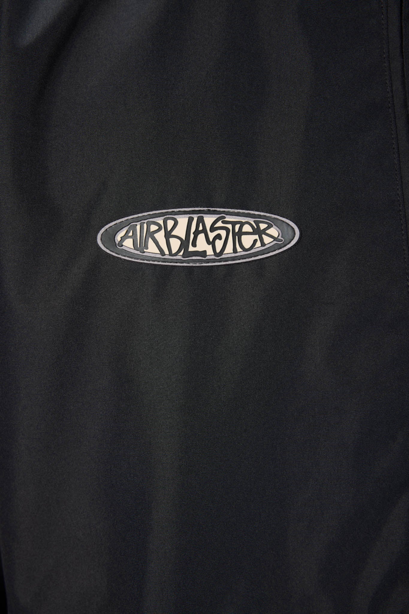 Close-up of a black garment featuring an oval embroidered Airblaster logo patch on the chest.