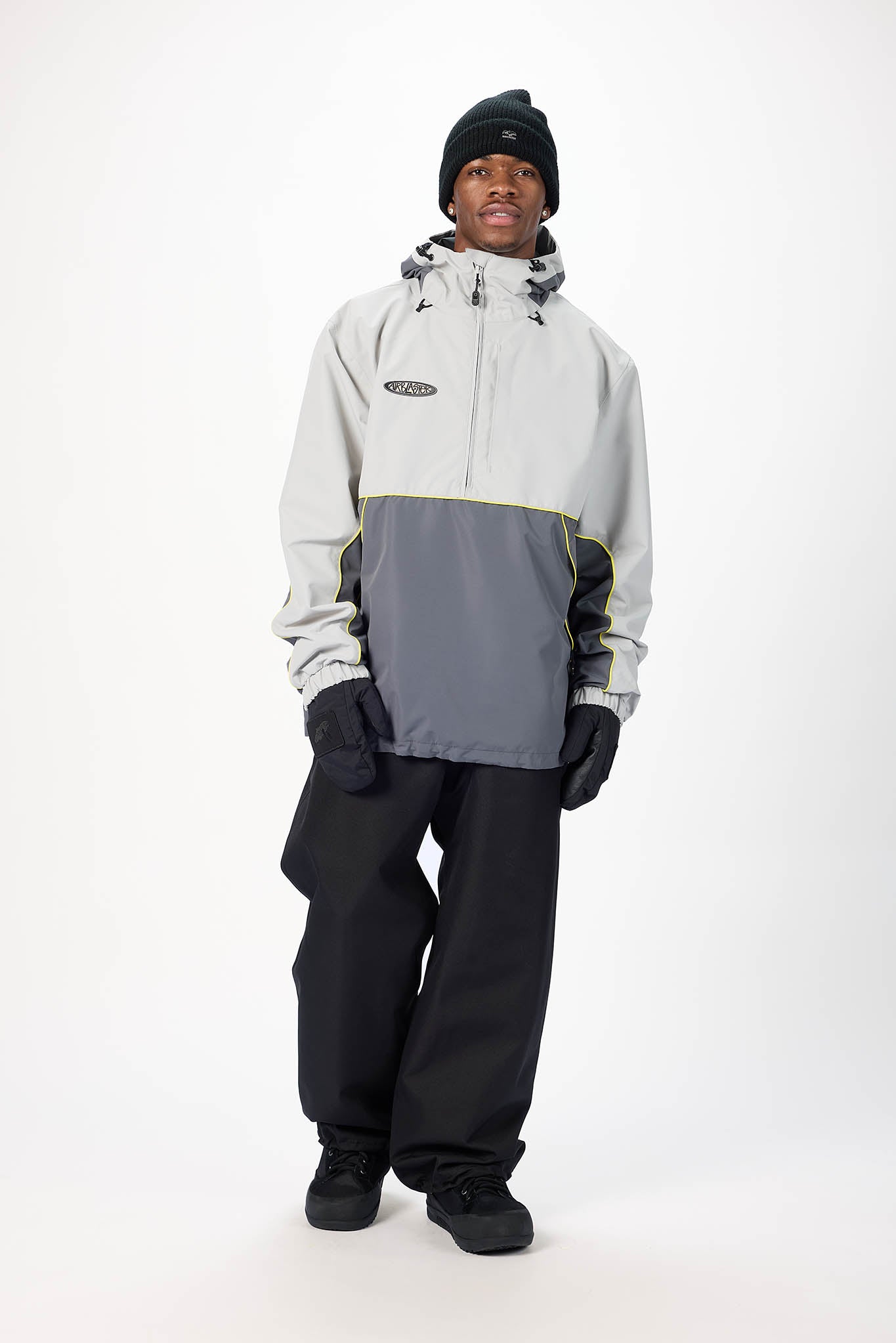 A man modeling a colorblock ski jacket with a light gray upper section, a dark gray lower section, and black gloves, pants, and beanie against a white studio background.