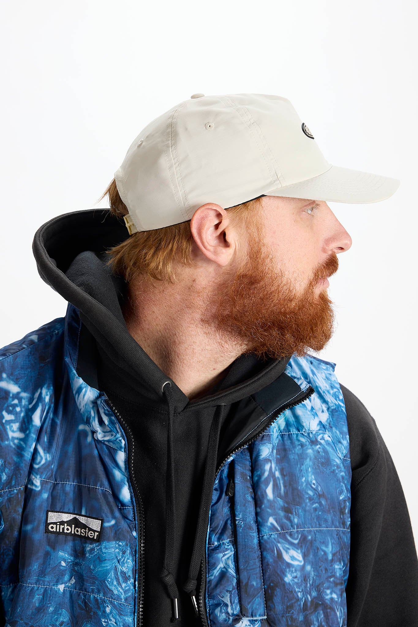 side profile A man with a red beard wearing a white baseball cap photographed against a plain white background.