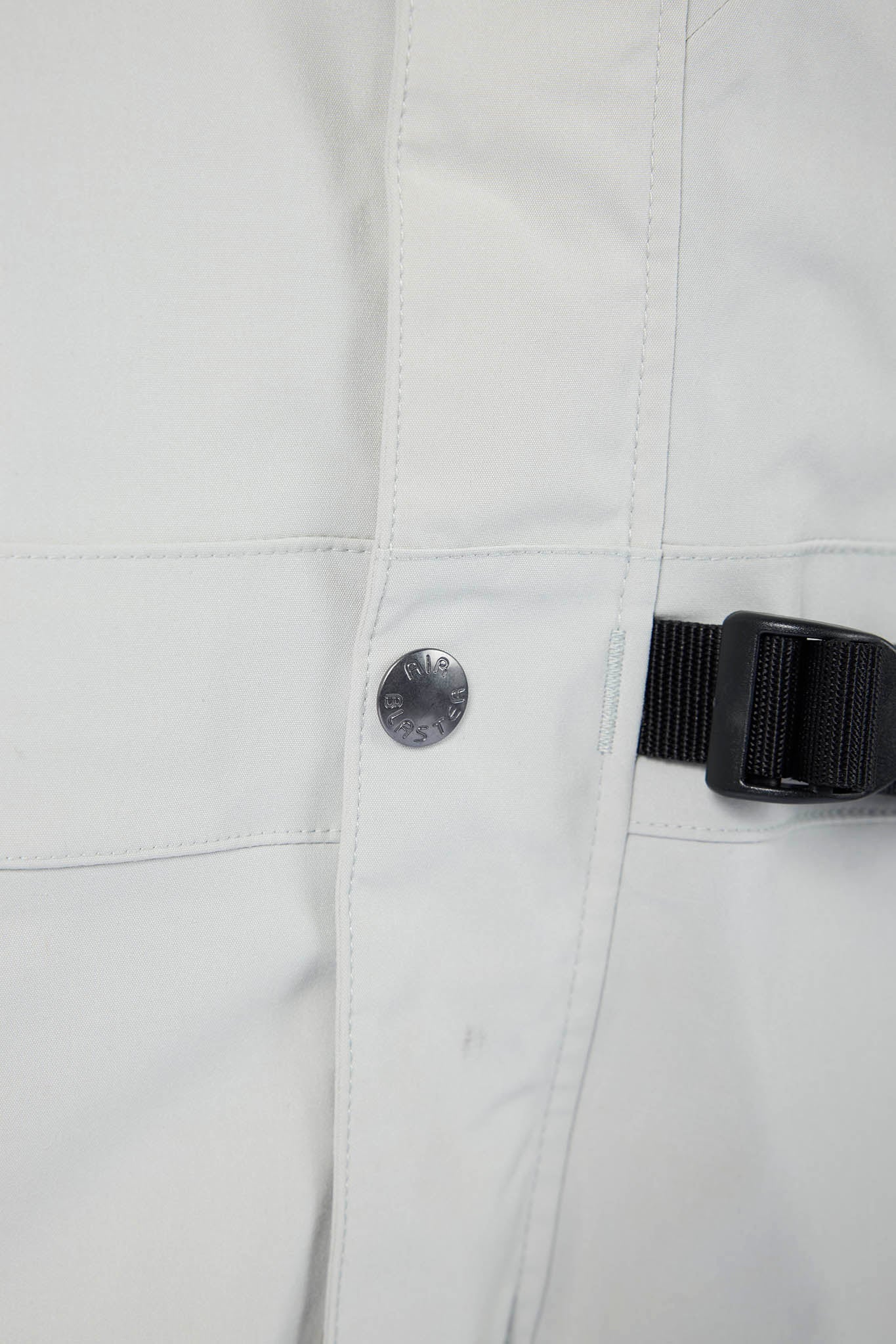 Close-up of a light gray jacket with a button and black strap on a white background