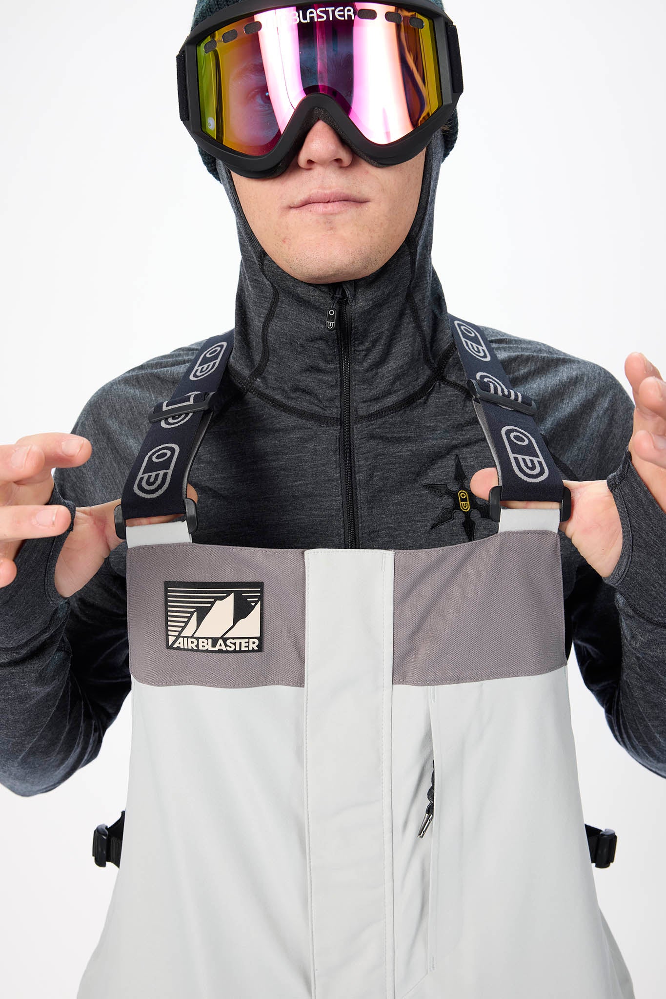 Person wearing a gray and white ski suit with goggles, standing against a white background.