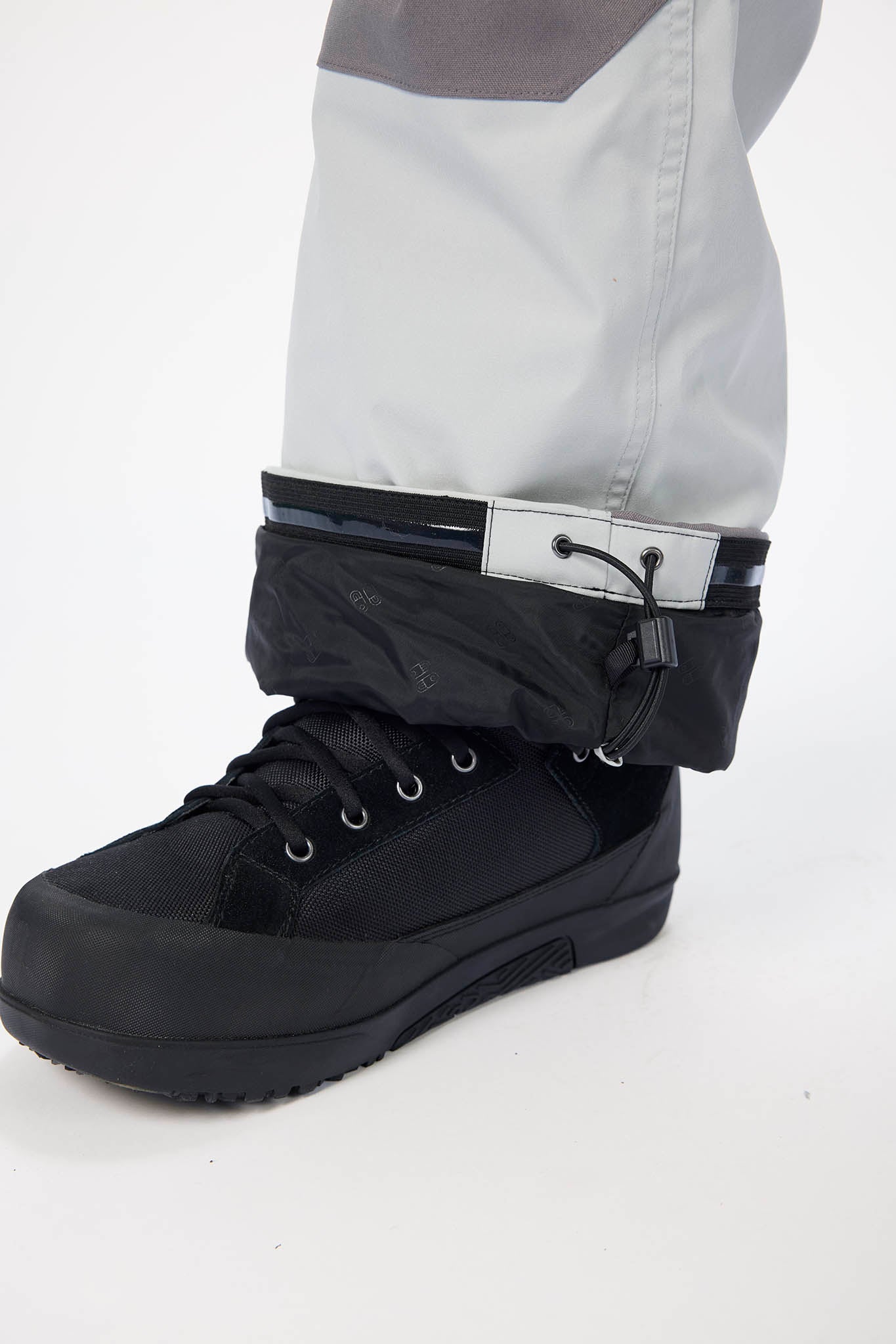 Black boot with gaiter worn over gray pants on a white background