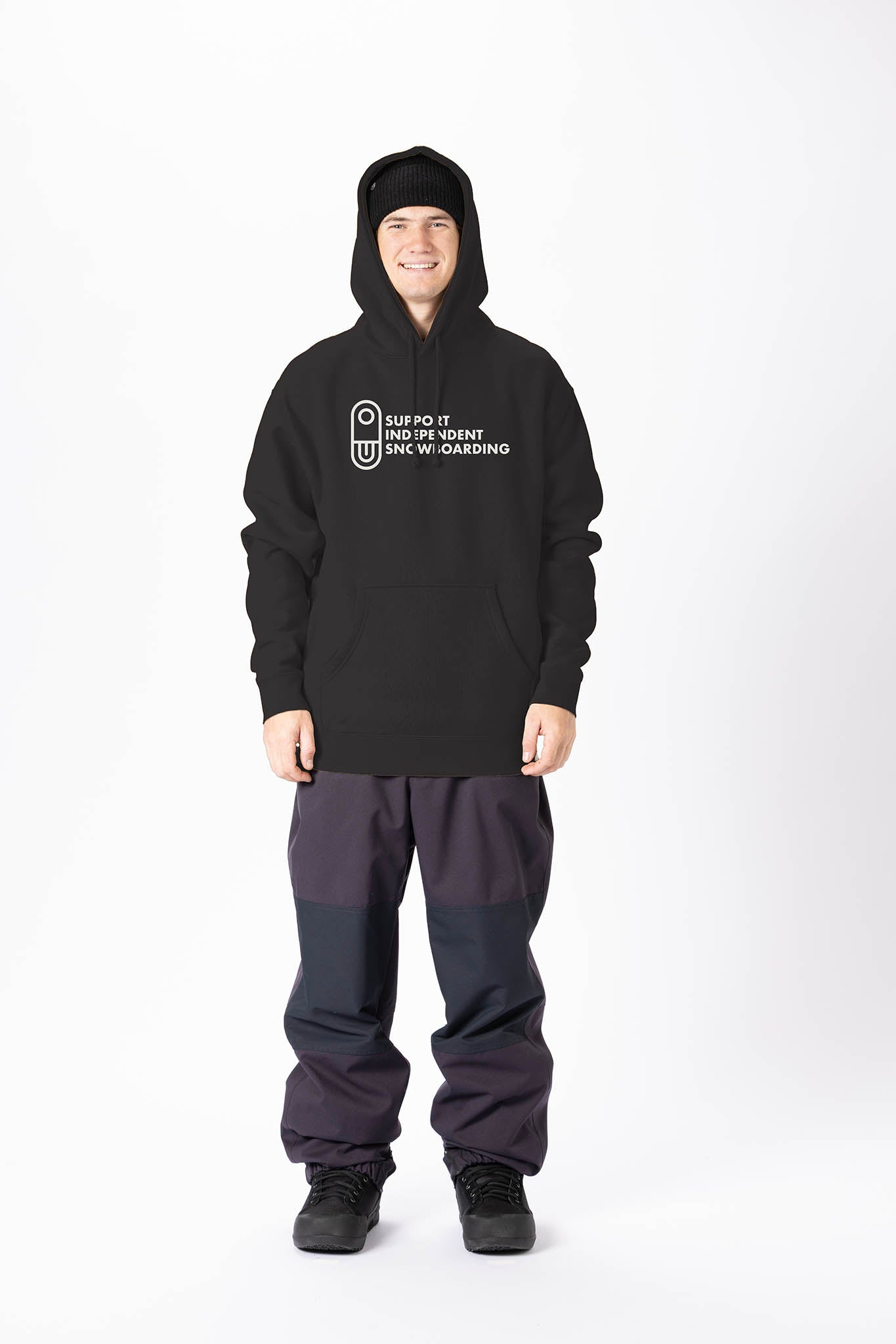 A man wearing a black pullover hoodie with a white printed graphic on the chest, paired with dark gray and black pants, standing against a plain white studio background.