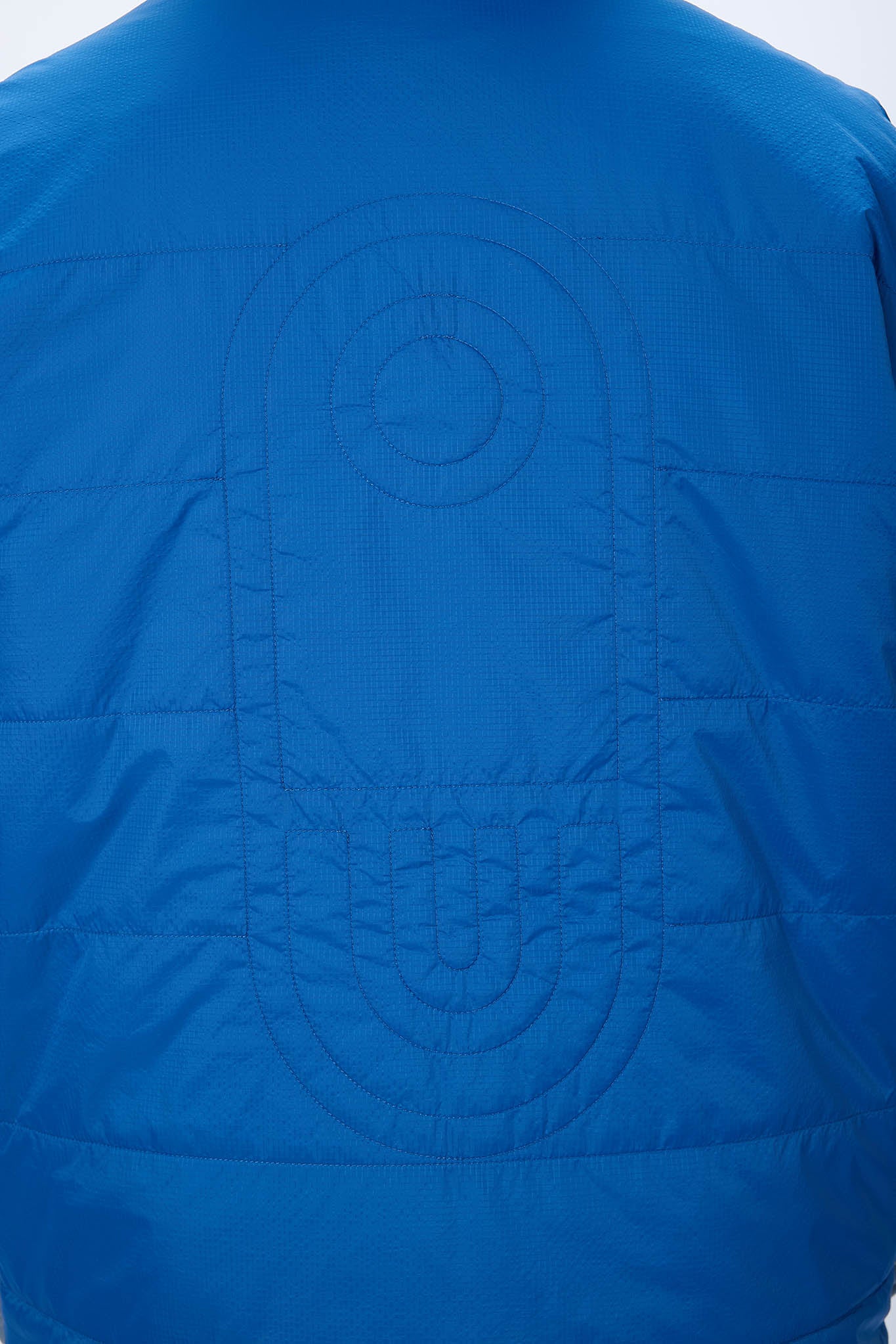 Close-up of a bright blue quilted puffer jacket showing the back panel with circular and oval quilting details.