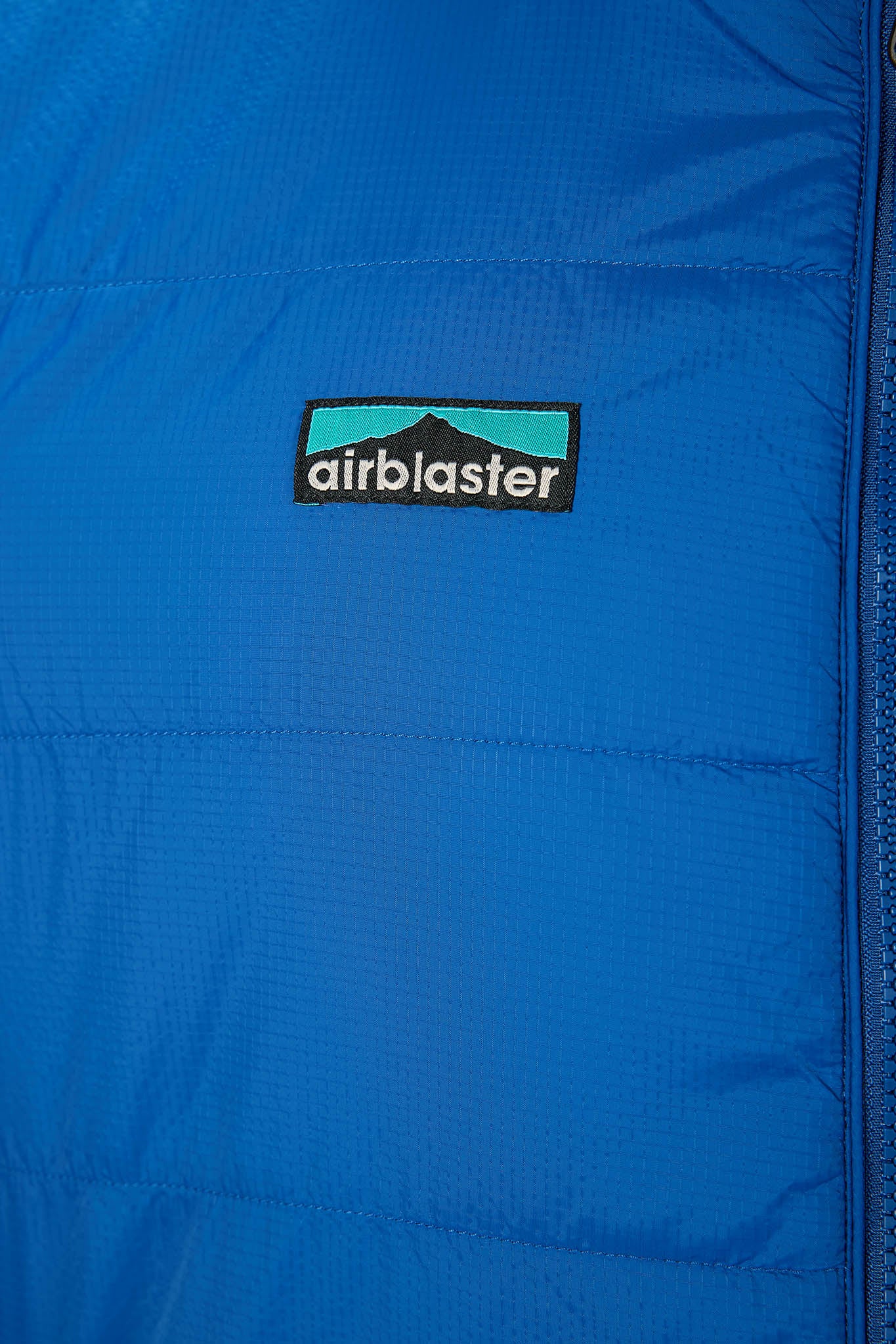 A close-up of a bright blue puffer jacket showing the black and teal Airblaster logo patch on the chest.