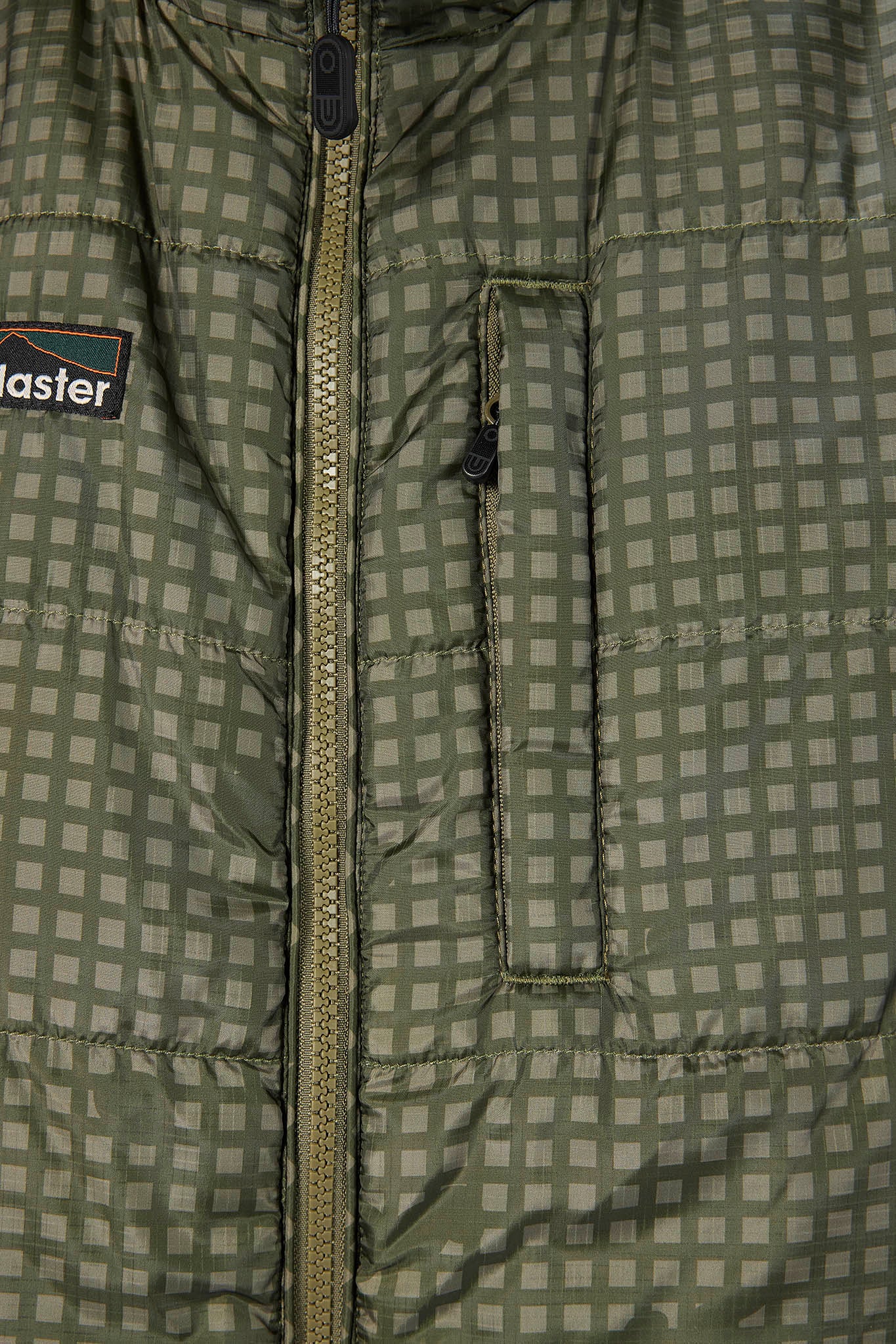 Close-up of a quilted jacket with a muted green and gray checkered pattern, a central zipper, and a visible Patagonia logo patch on the left chest.