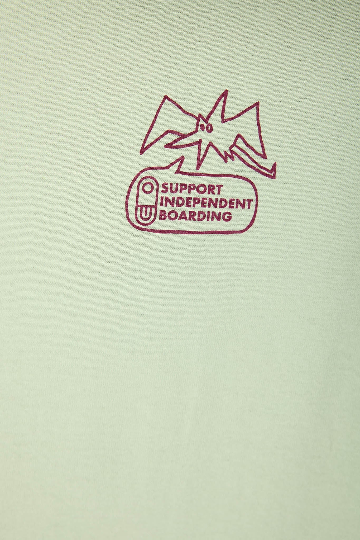Close-up of a off white fabric with a purple screen-printed graphic that reads 'SUPPORT INDEPENDENT BOARDING' beneath a stylized outline.