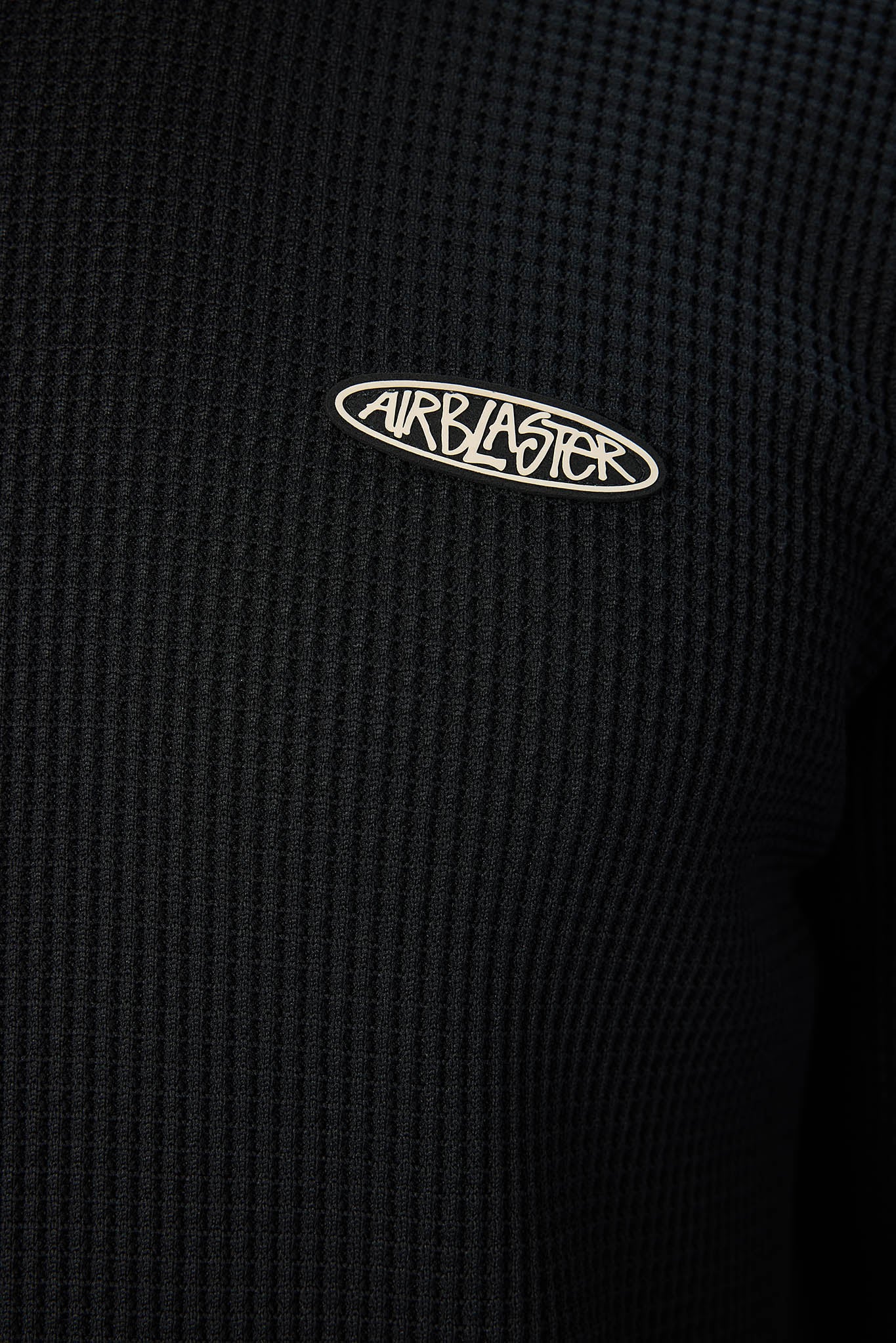 Close-up of a black waffle-knit garment with a small white oval Airblaster logo on the chest.