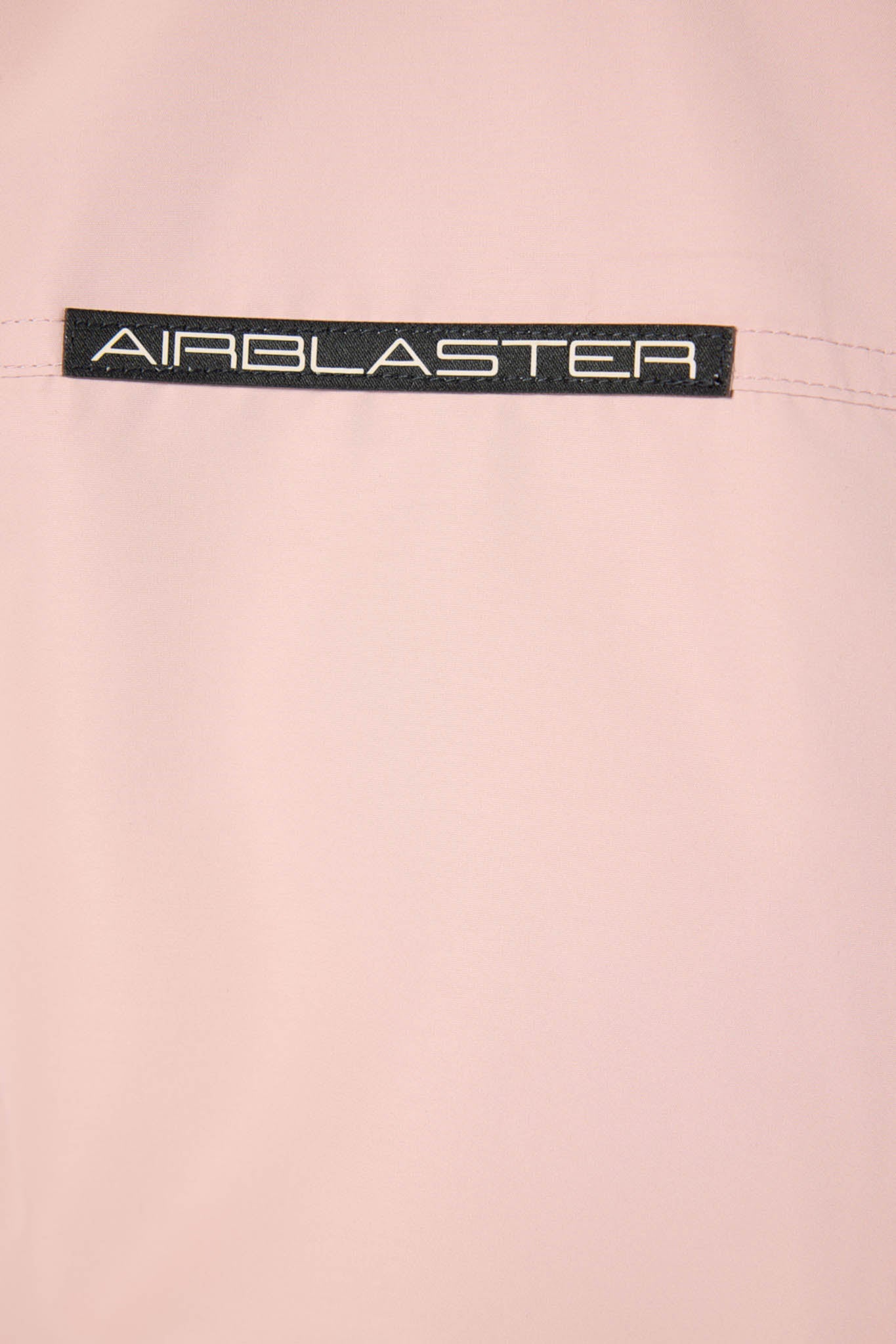 Close-up of a pink fabric with 'AIRBLASTER' logo on a light pink background