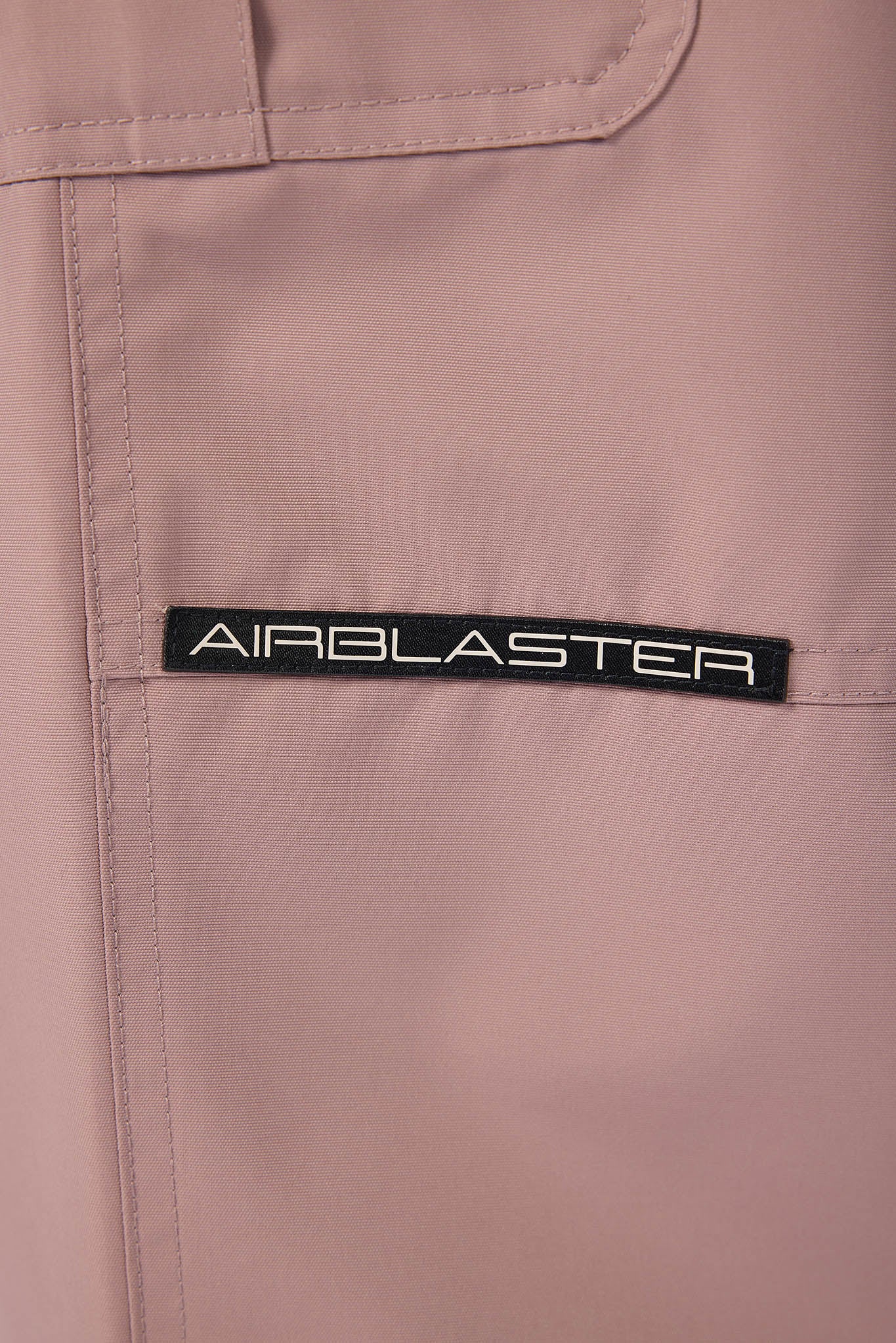 Close-up of a brown jacket with 'AIRBLASTER' logo on a beige background