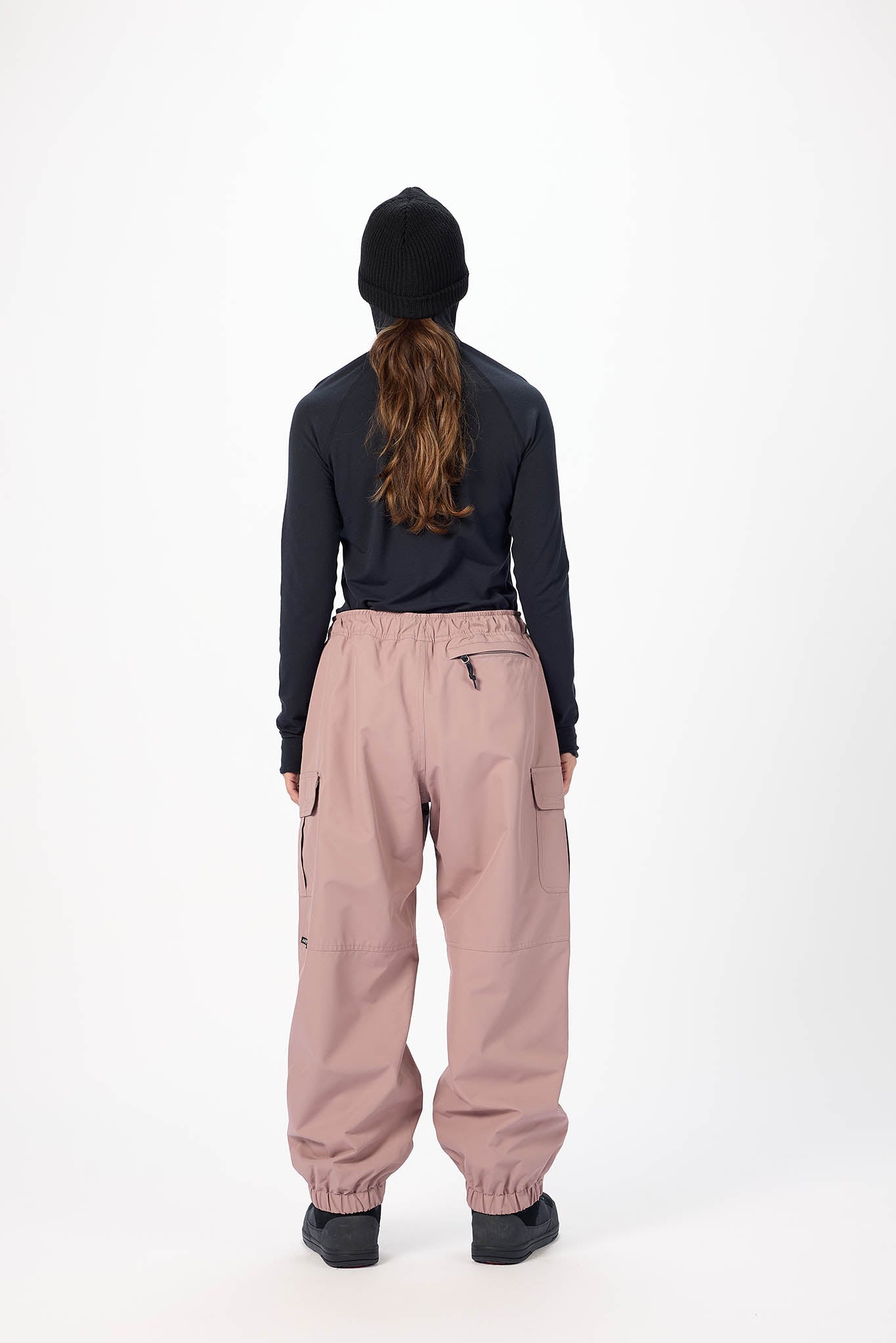 Person wearing a dark long-sleeve top and light pink pants on a white background