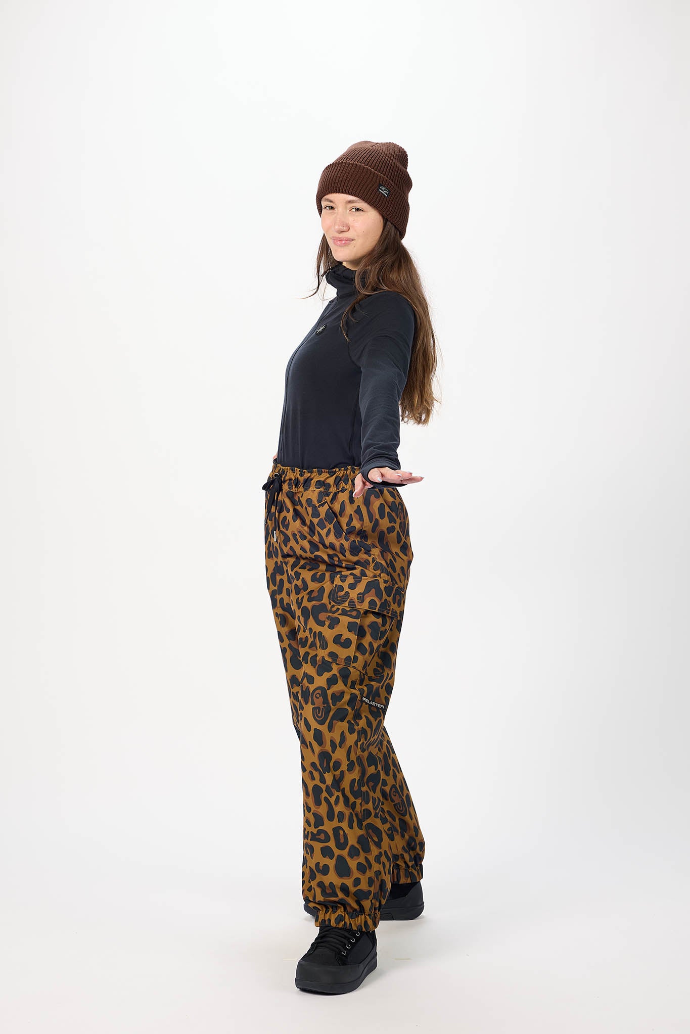 Person wearing a black top, leopard print pants, and a brown beanie on a white background