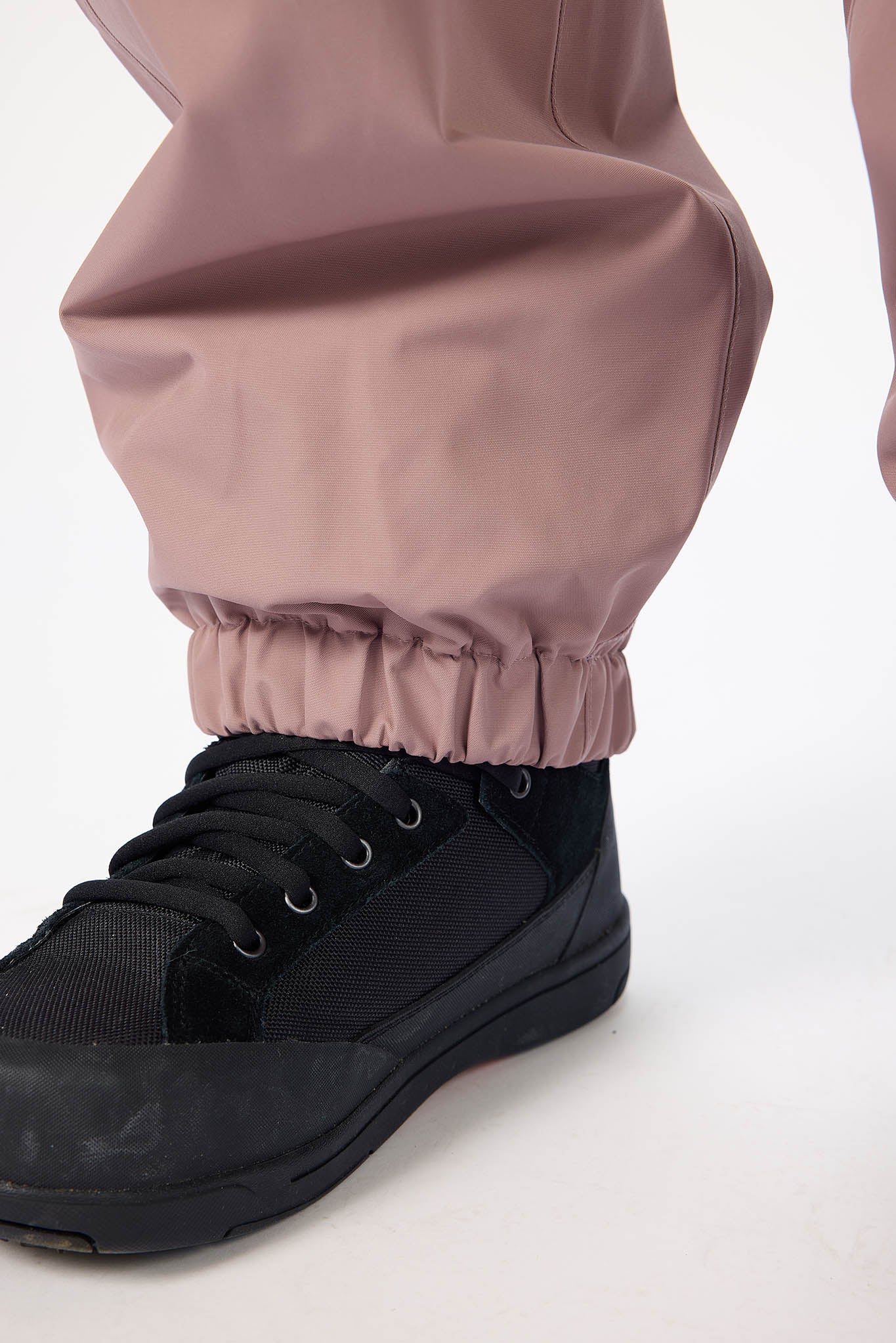 Close-up of a black shoe with a pink legging on a white background