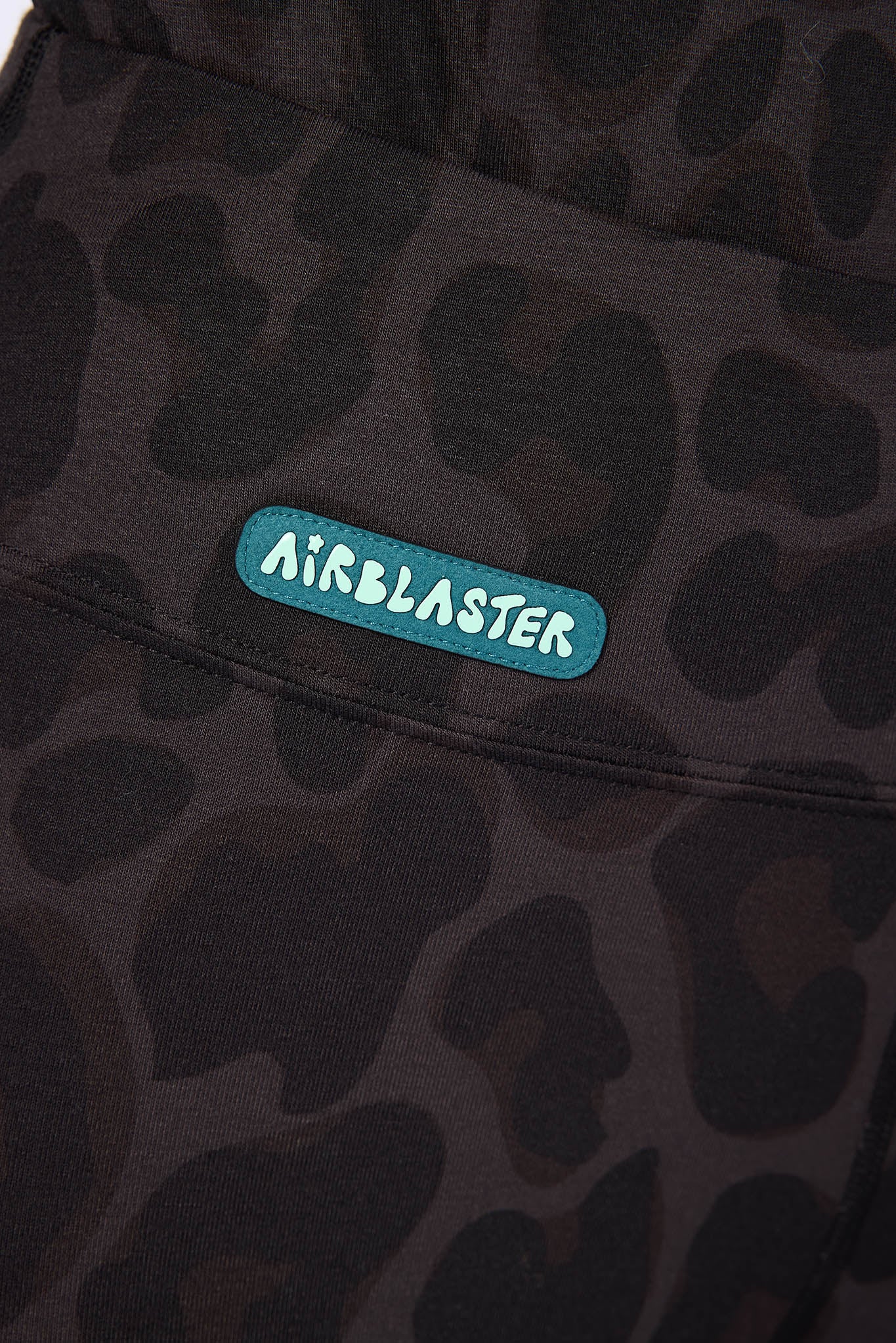Close-up of a dark brown and black camouflage-patterned garment featuring a teal Airblaster patch on the chest.