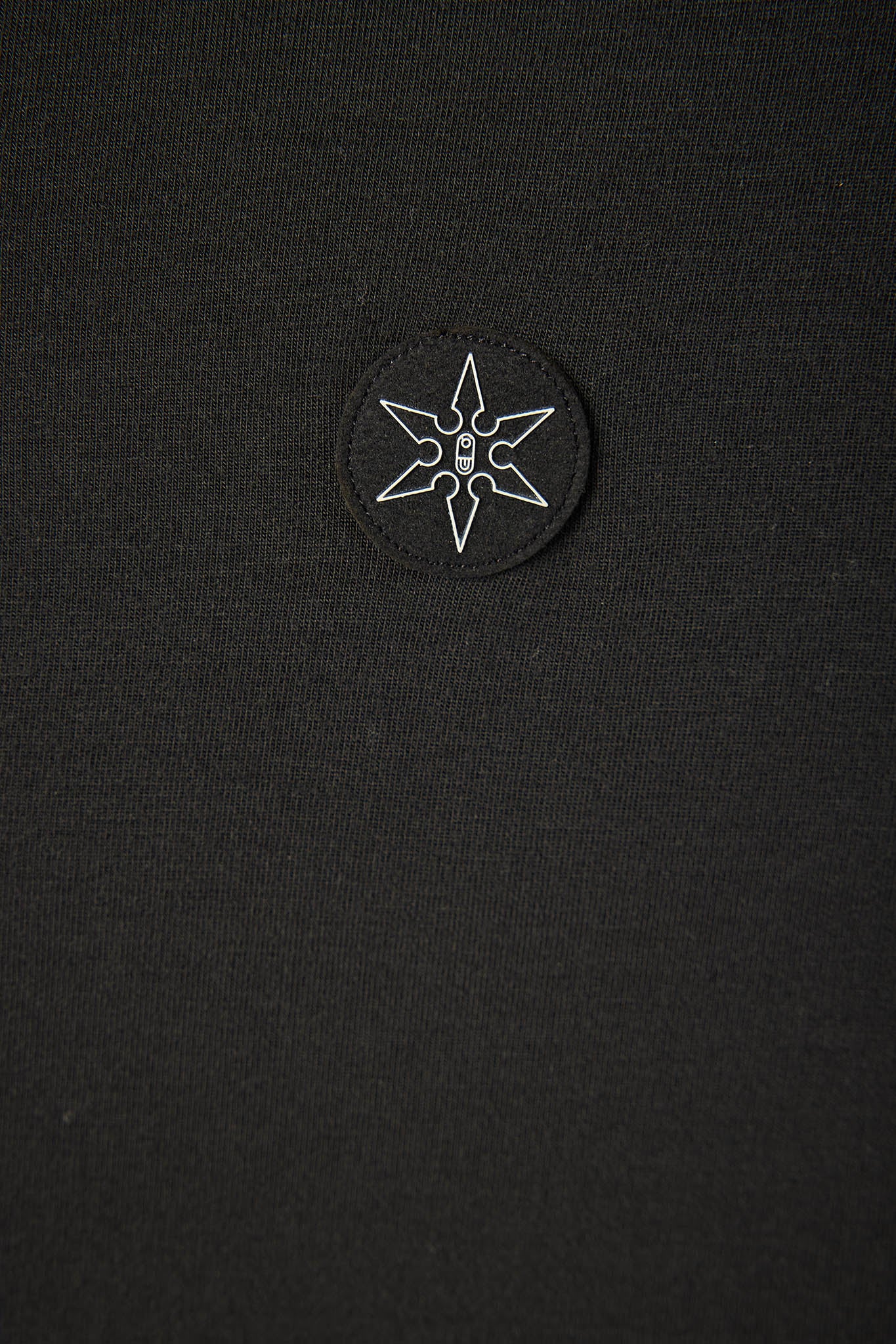 Close-up of a black knit garment featuring a circular black patch with a white outlined six-pointed star logo on the chest.