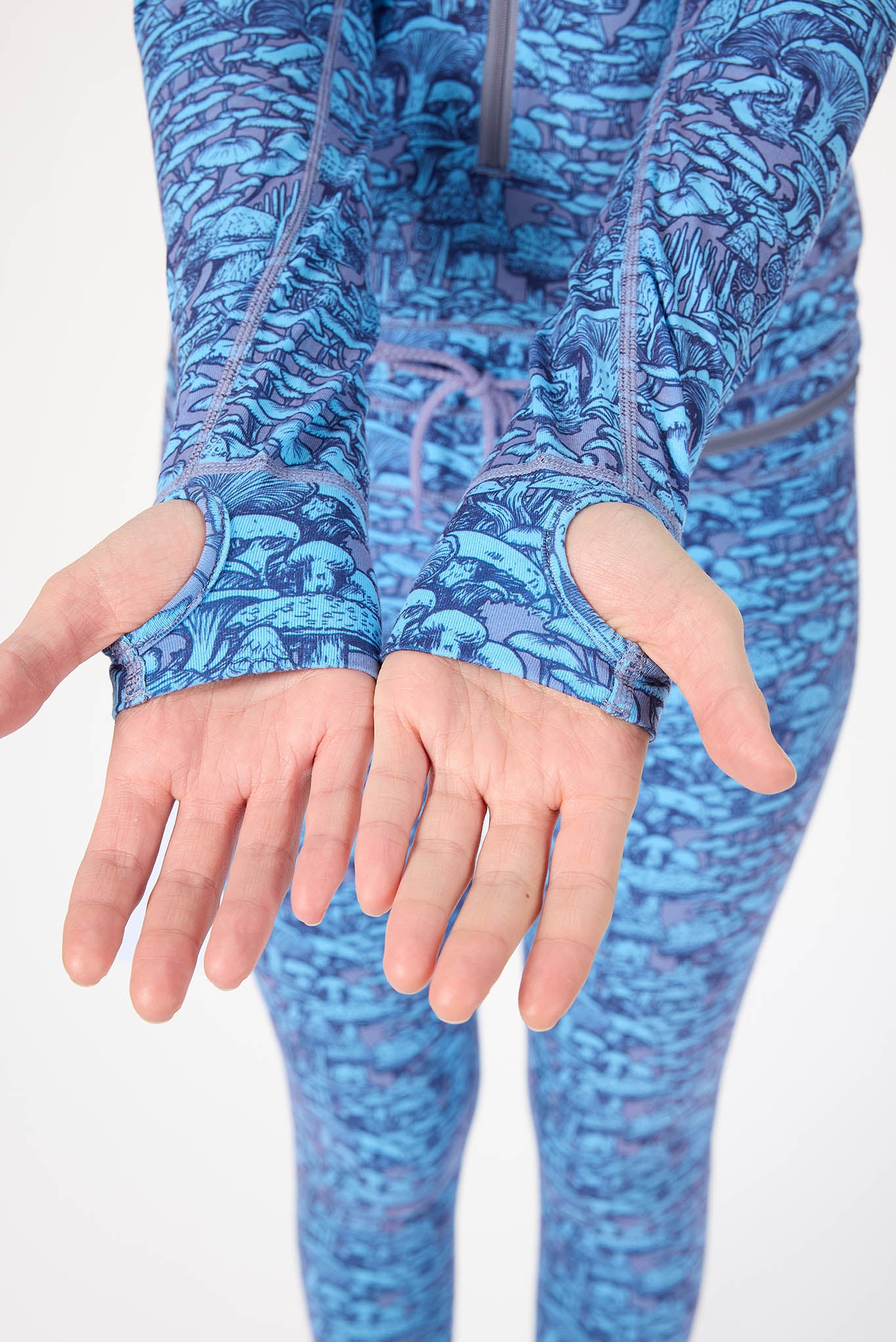 A close-up of a person wearing a blue and purple patterned long-sleeve athletic top and matching leggings, with both hands extended forward showing the wrist openings.