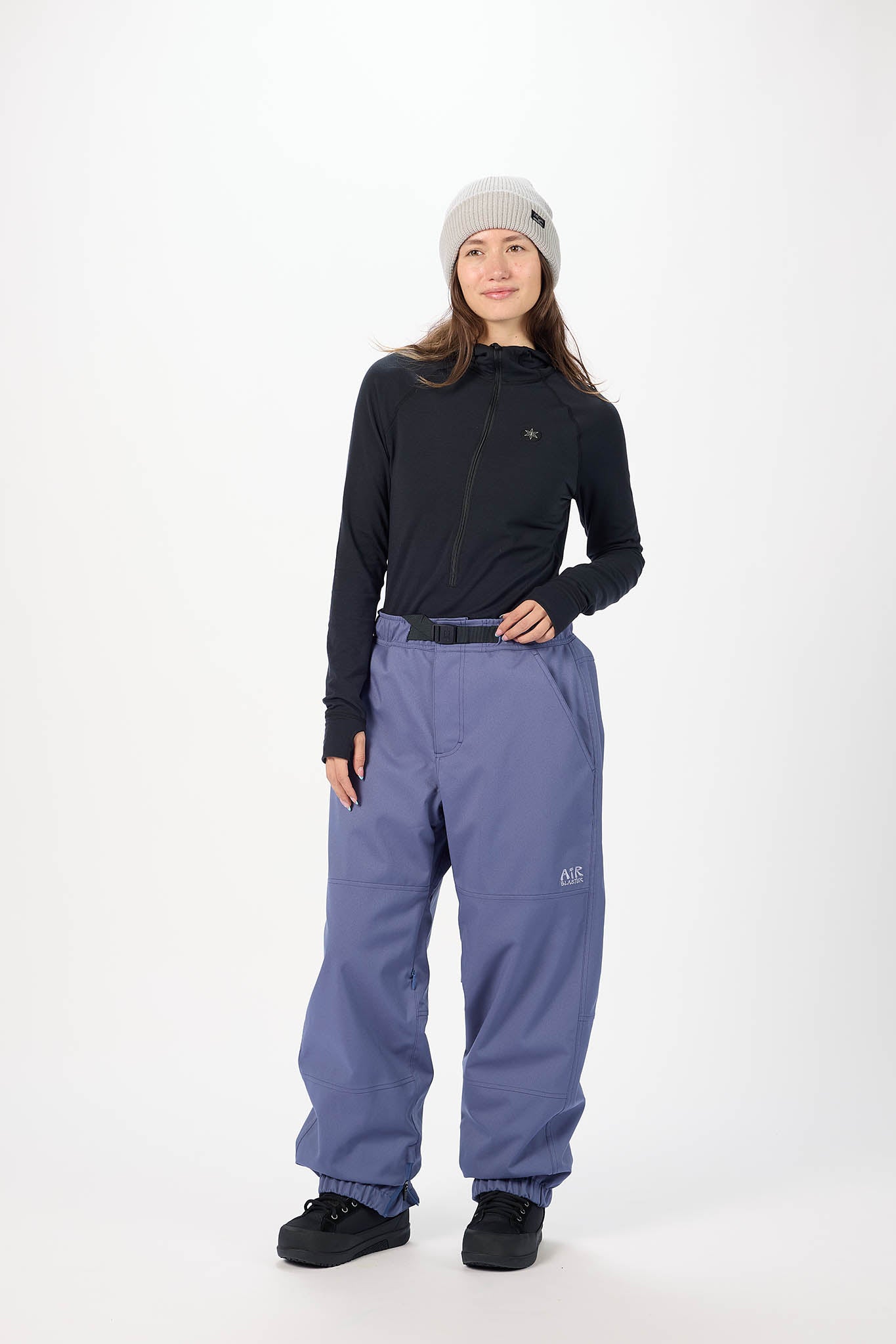 Person wearing a black long-sleeve top and blue snow pants on a white background