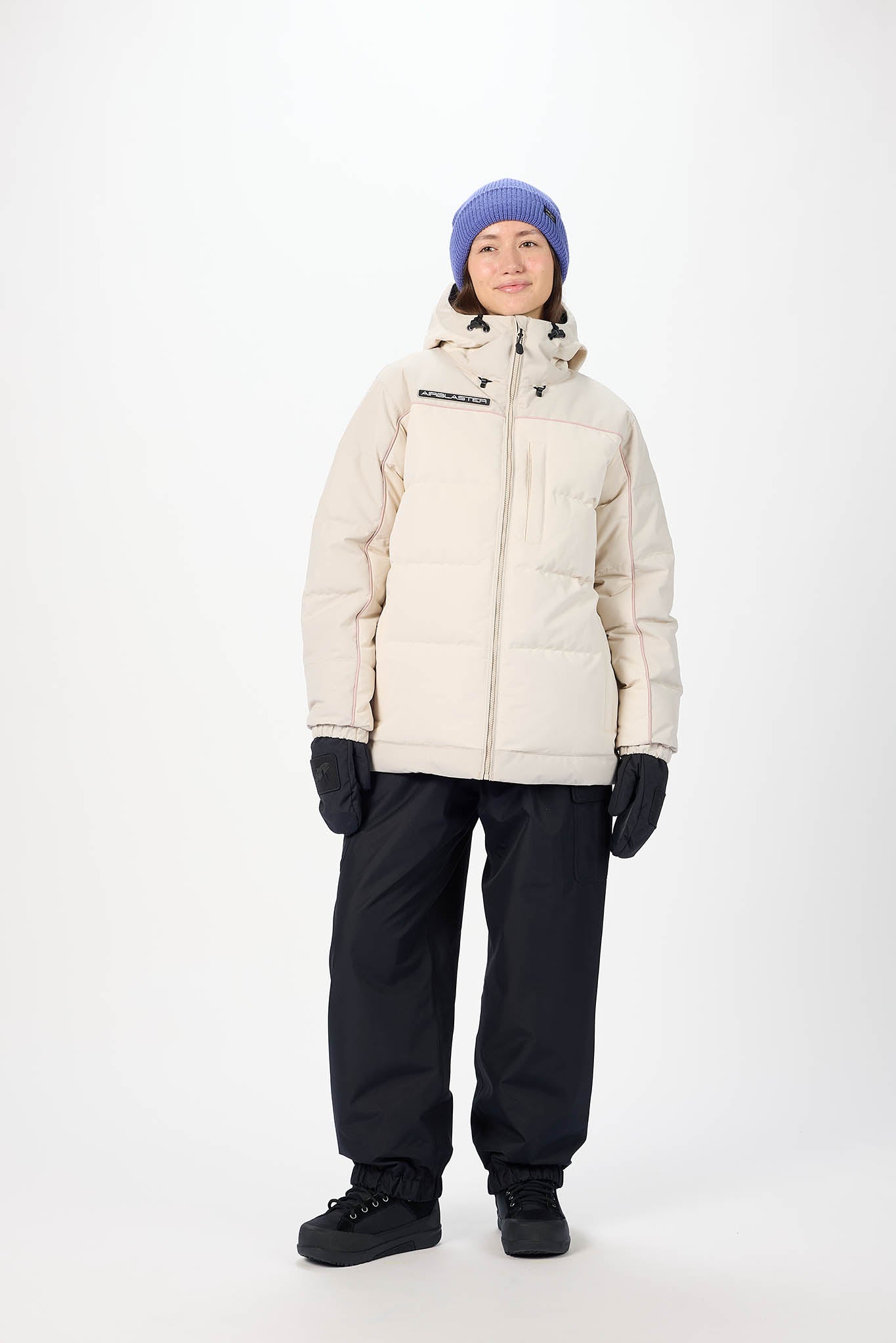 Person wearing a beige puffer jacket, black pants, and a blue beanie on a white background