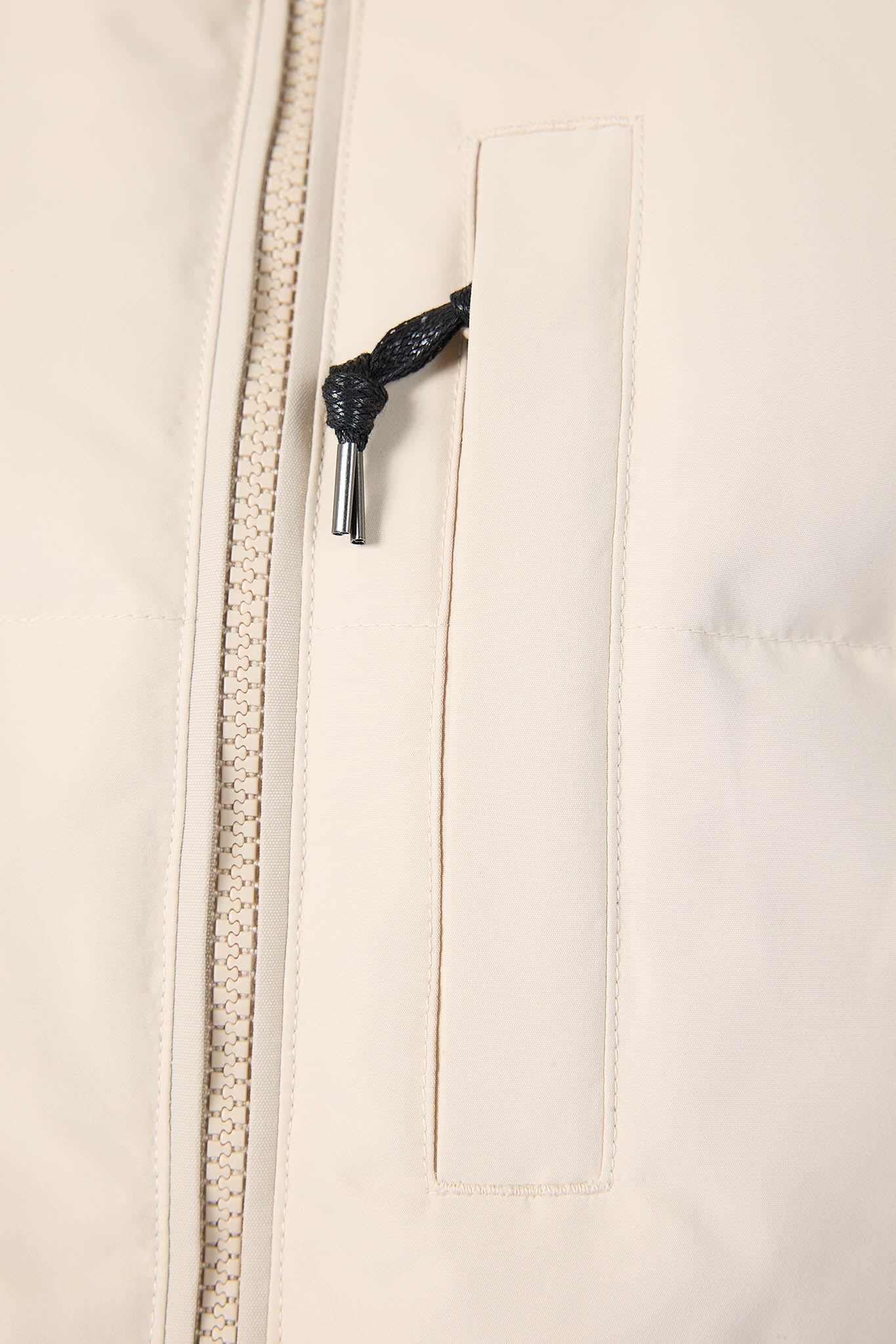 Close-up of a beige jacket zipper with a black pull tab on a beige background