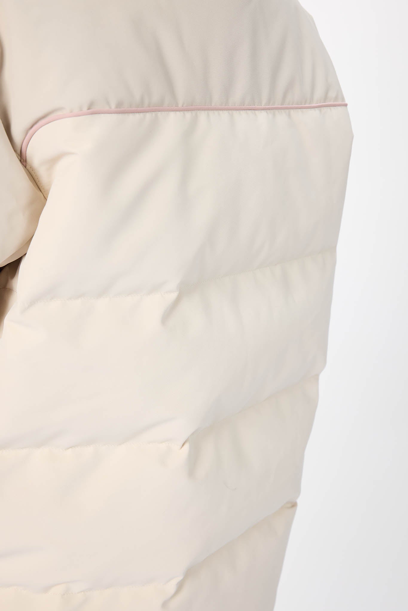 Close-up of a beige quilted jacket with pink stitching on a white background