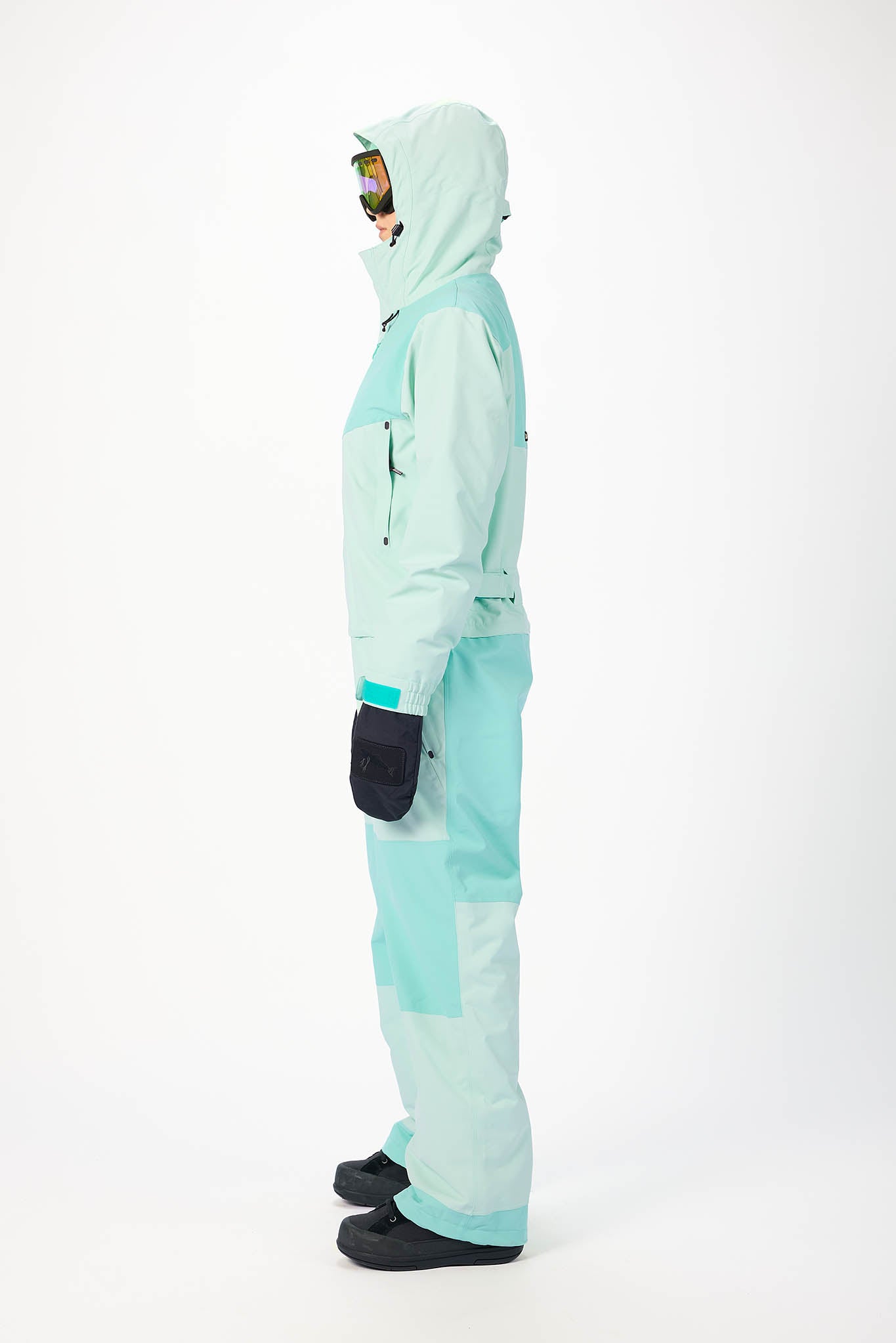 Person wearing a mint snowsuit on a white background in side profile