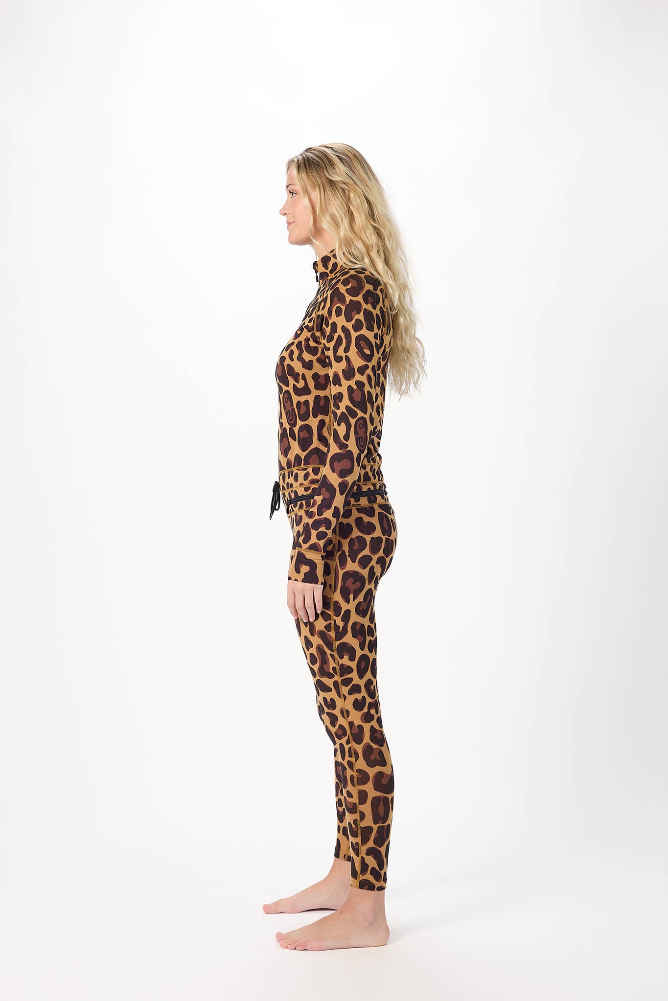 A woman standing in profile wearing a leopard-print long-sleeve top and matching leggings against a plain white studio background.