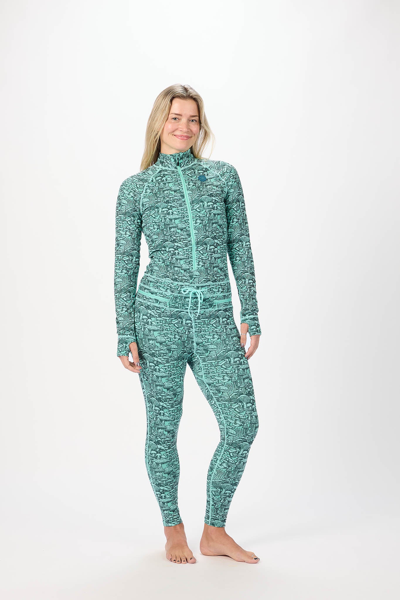 A woman modeling a matching two-piece activewear set featuring a high-neck long-sleeve zip-up top and coordinating leggings, both in a green and white heathered pattern, against a plain white studio background.
