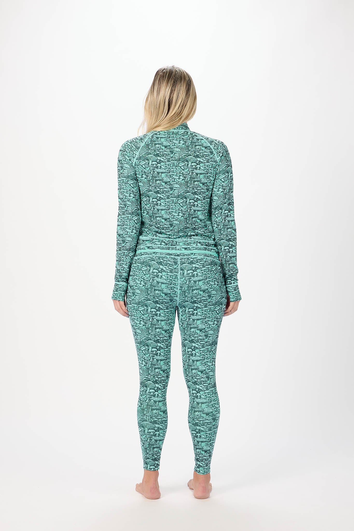 A woman viewed from behind wearing a matching long-sleeve top and leggings set in a textured teal and mint green pattern, standing against a plain white studio background.