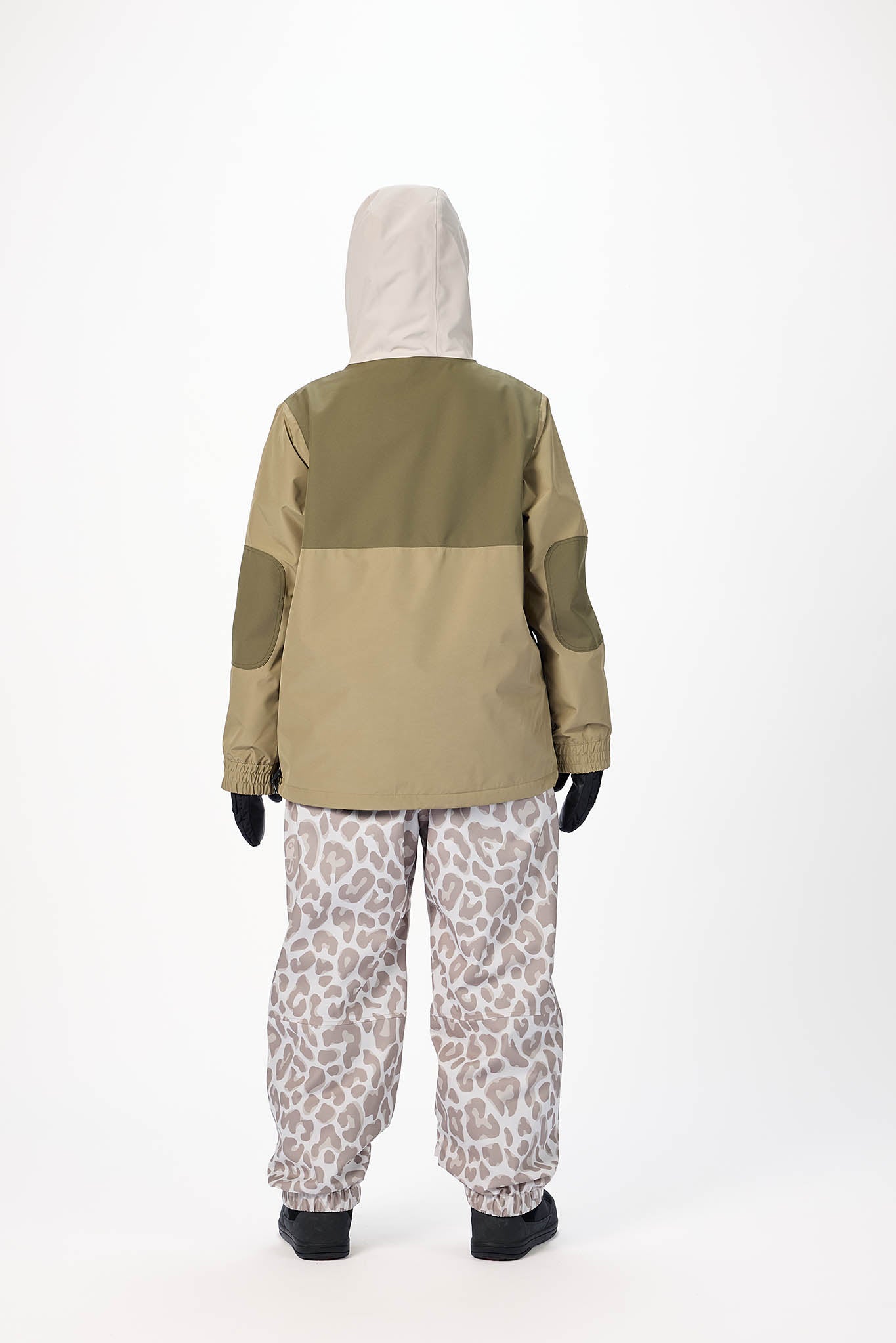Person wearing a green and beige jacket with a hood, standing against a white background