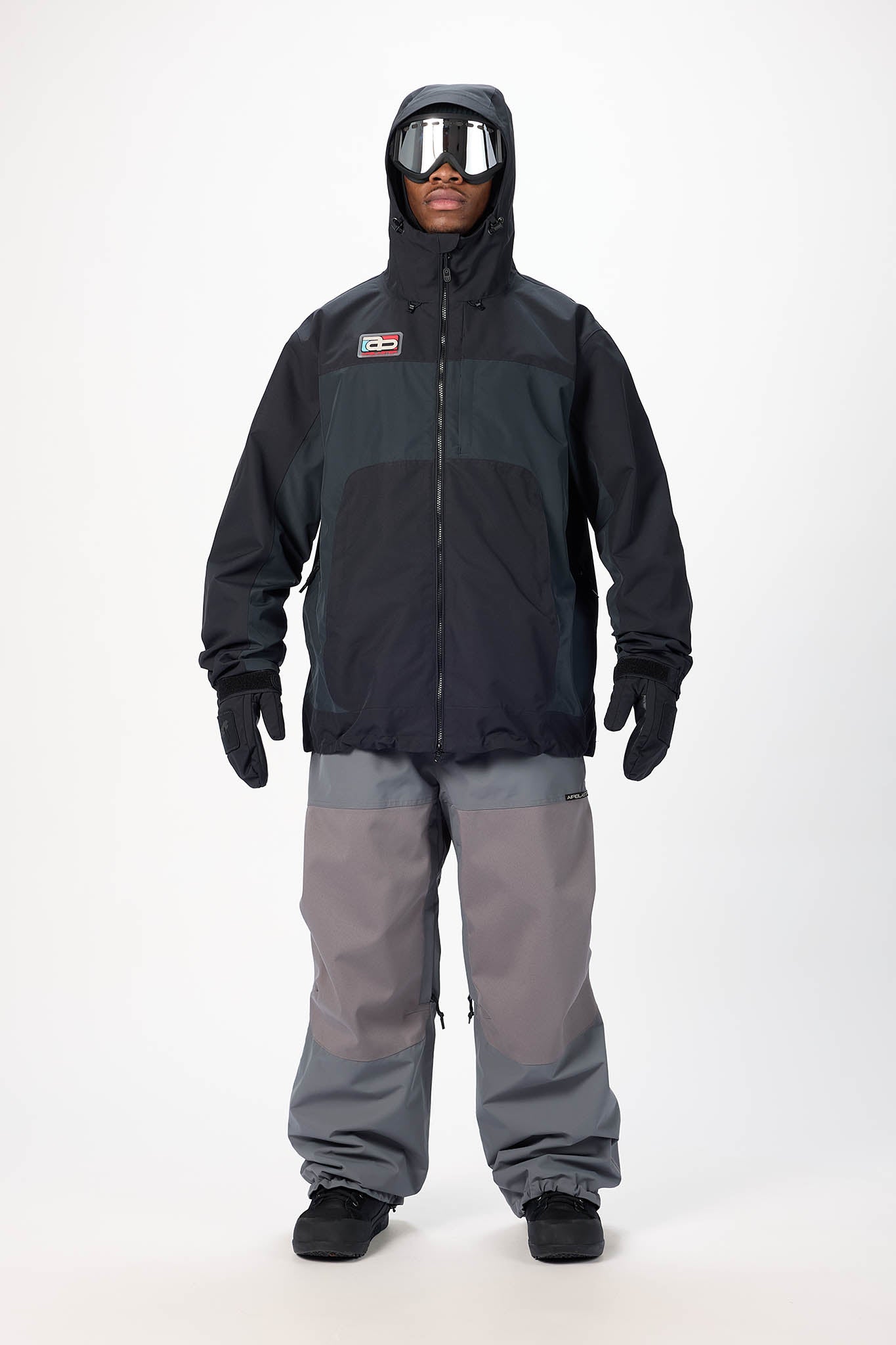 Person wearing a black and gray snowsuit with goggles on a white background
