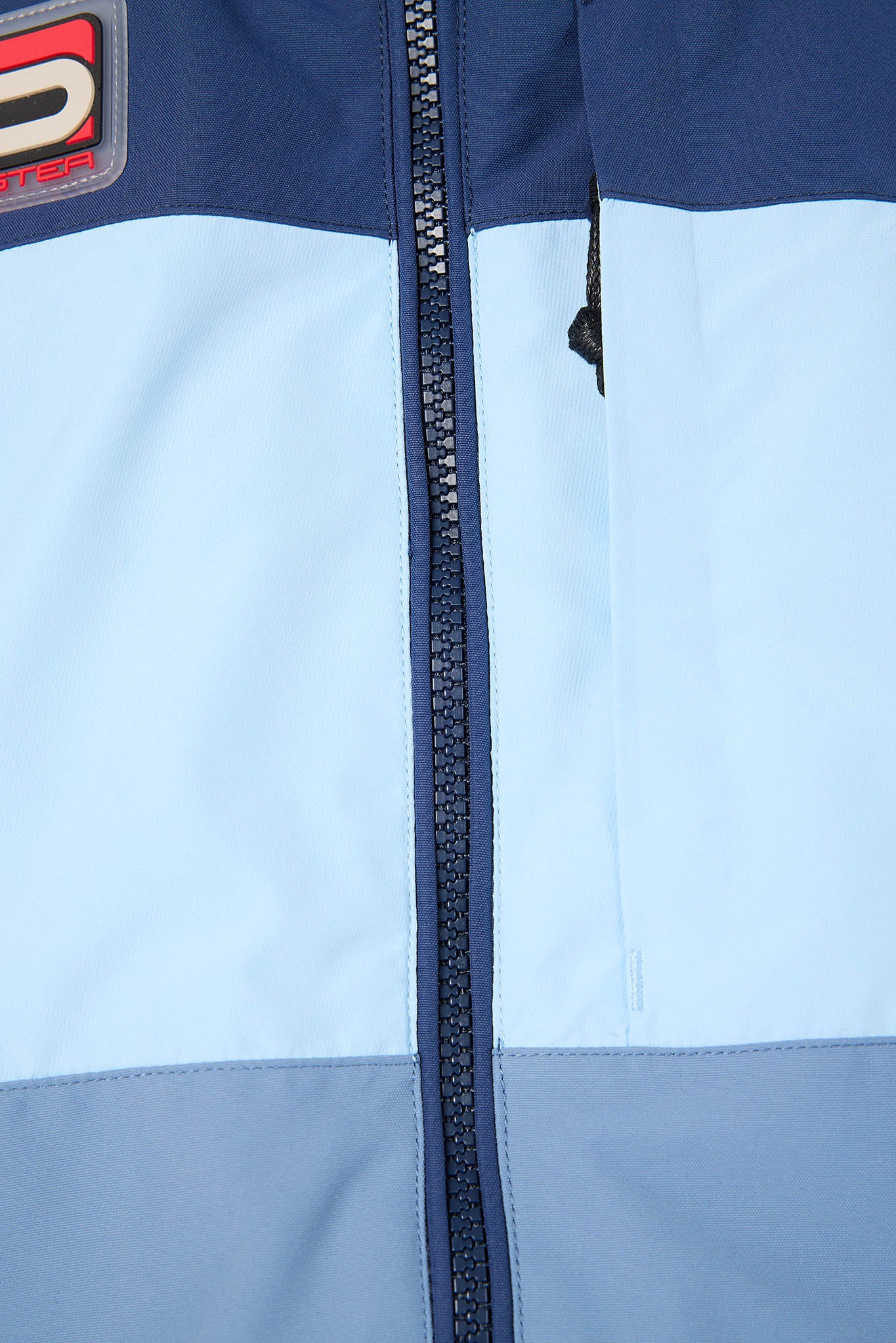 Close-up of a jacket with a zipper and brand logo on a light blue background