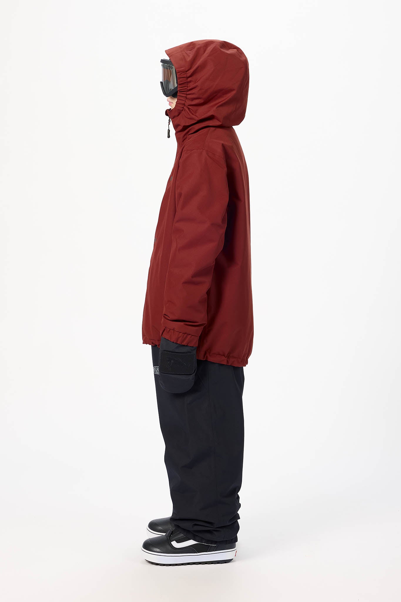 A side profile view of a person wearing a dark red hooded jacket, black pants, and black sneakers against a plain white studio background.