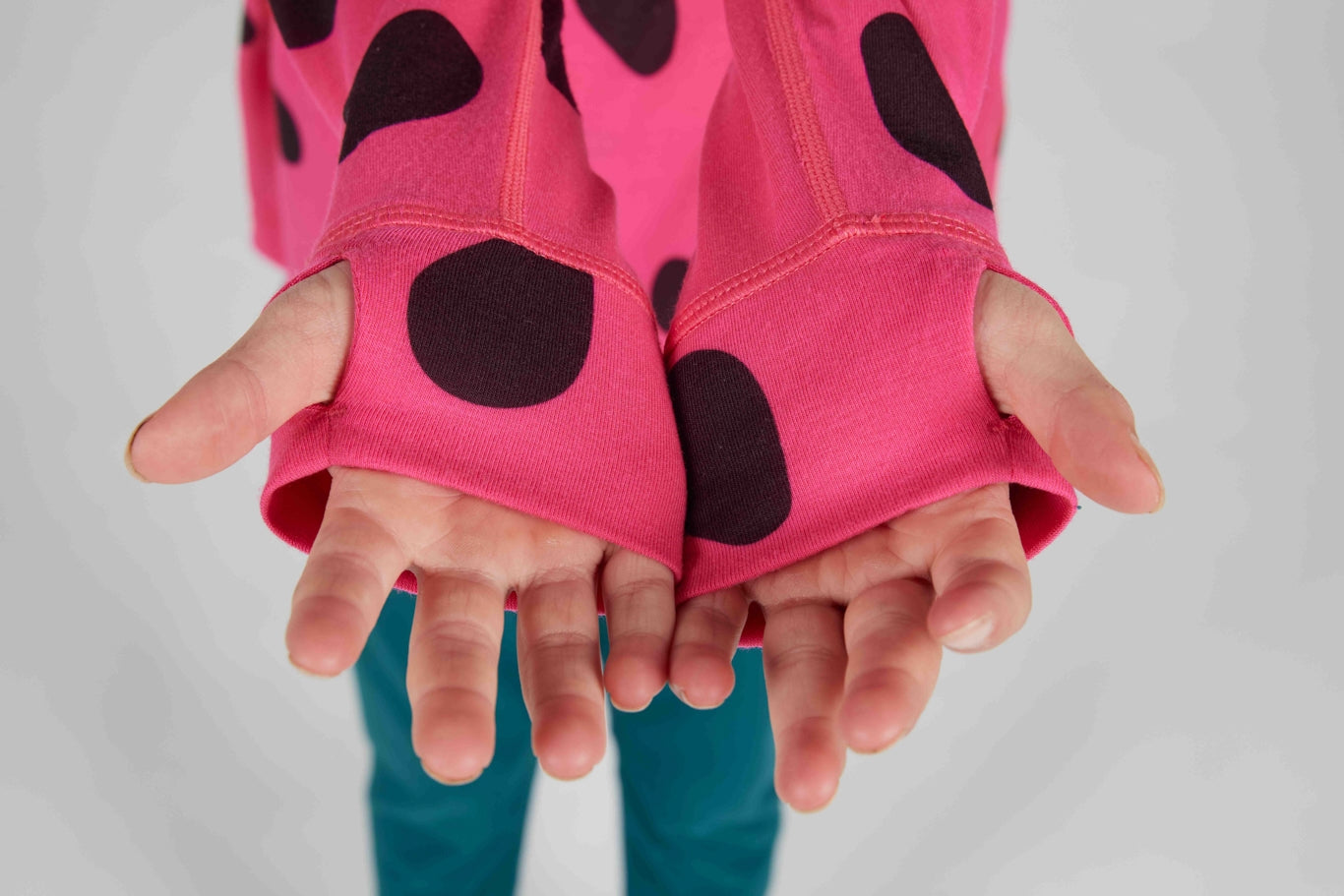 Close-up of a person's hands wearing bright pink fingerless gloves with large black polka dots, against a light gray background.