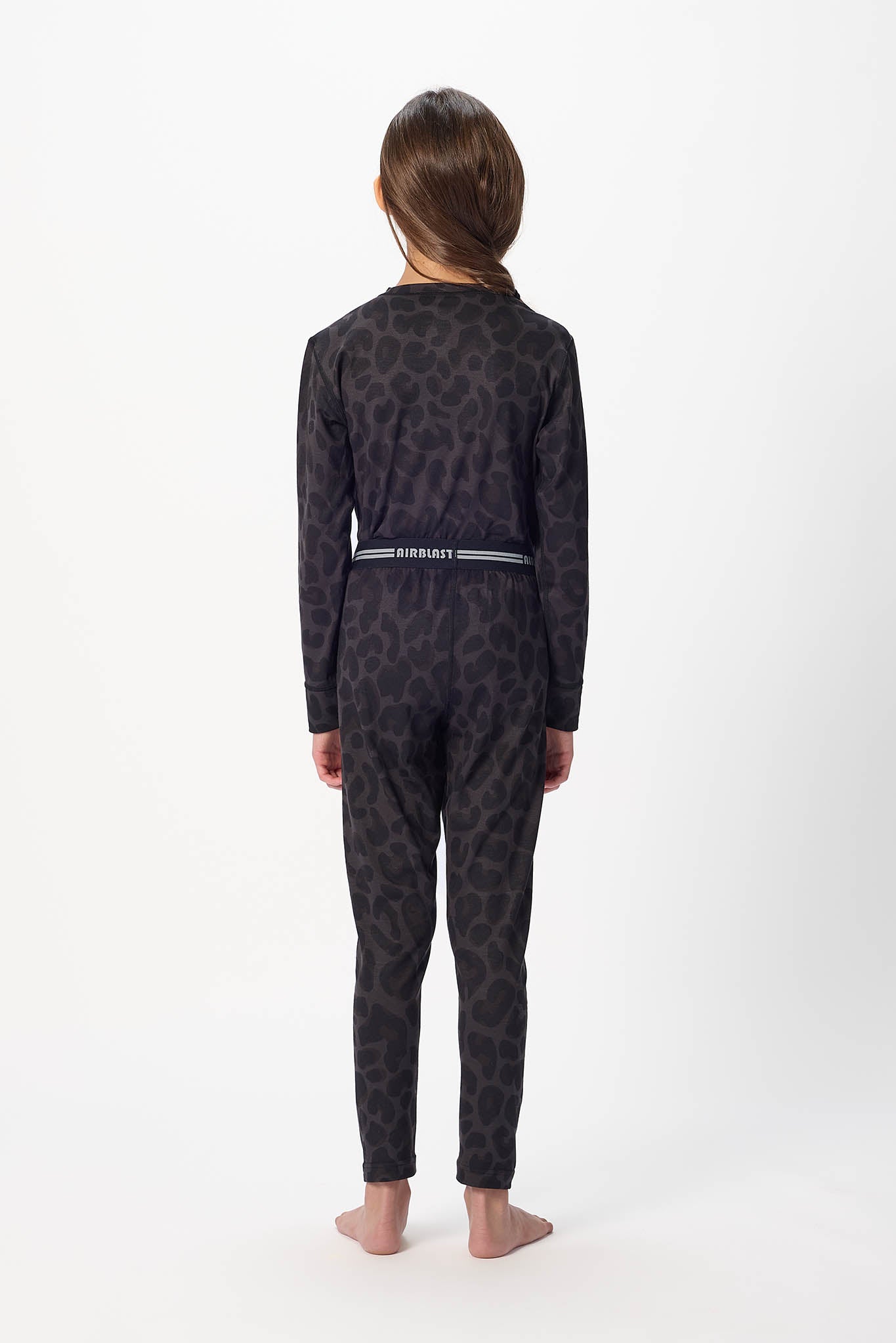 Youth model wearing Black leopard base layer bottoms,standing with back facing the camera with a white background.