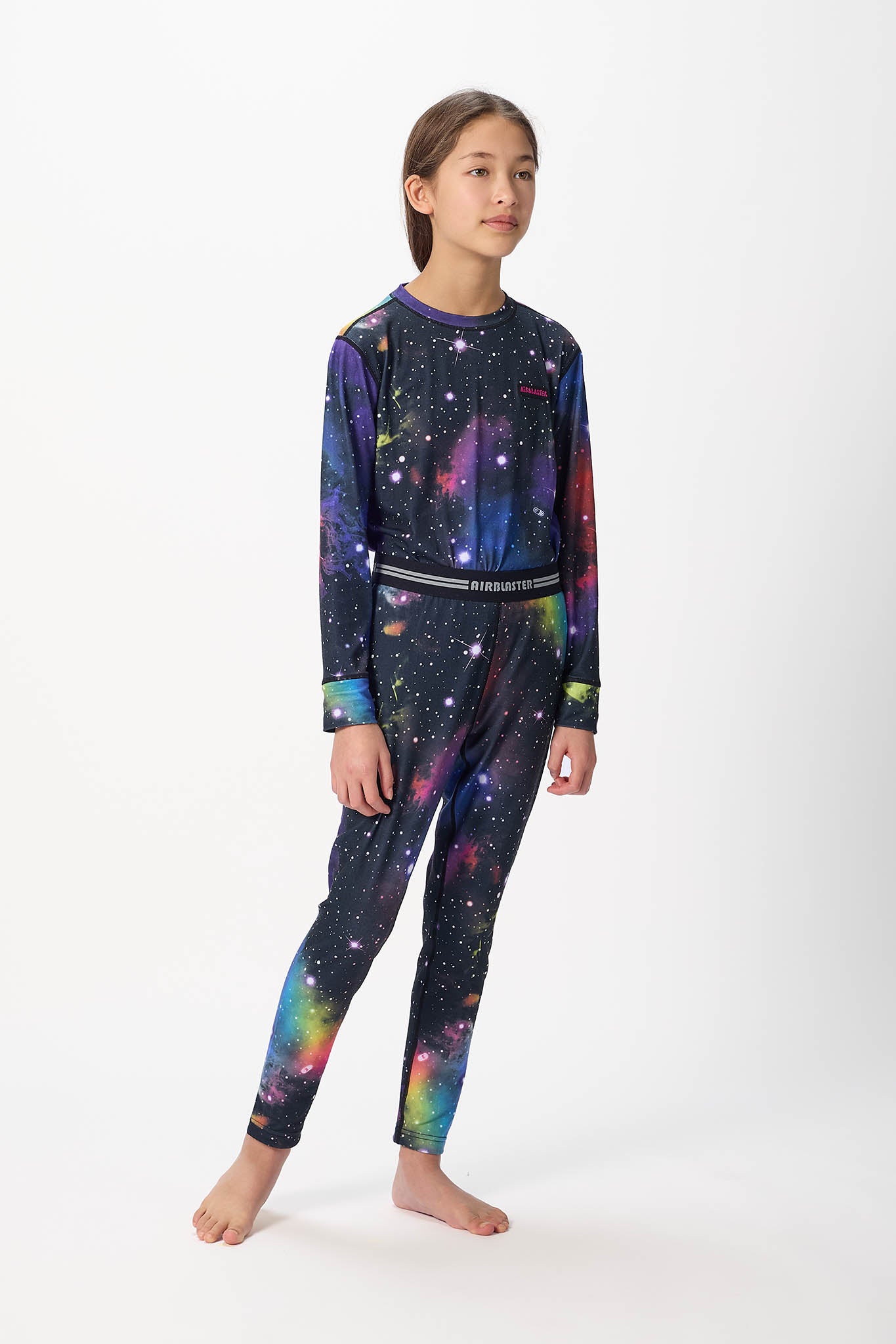 Youth standing center frame, looking away wearing black with far out , youth base layer bottoms with white background.