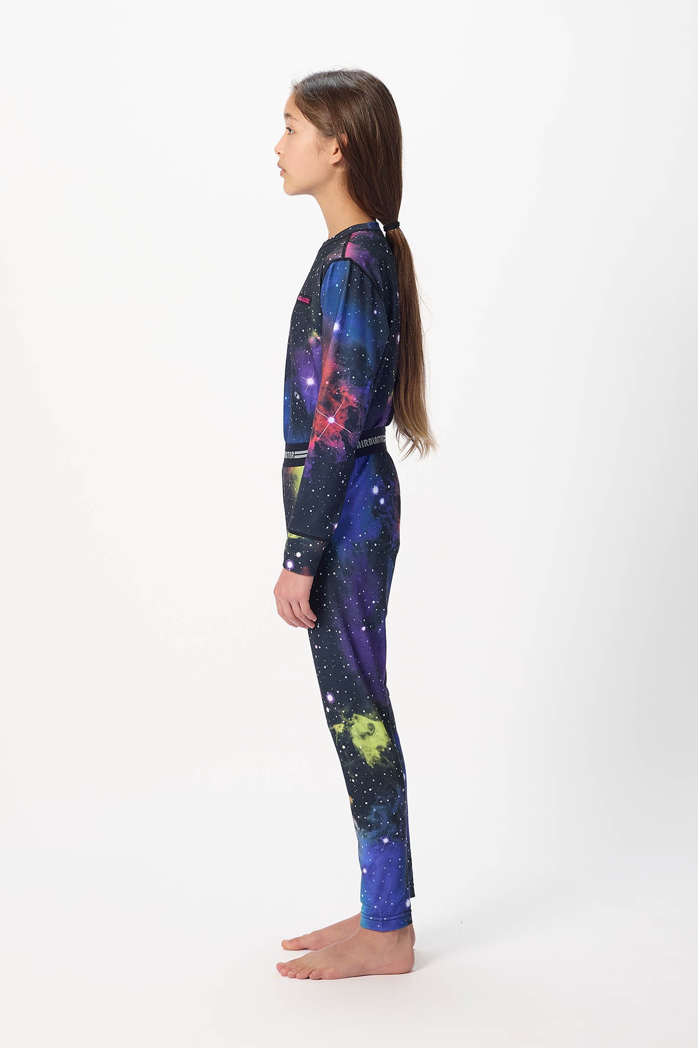 Youth model wearing black with Far Out base layer bottoms,standing sideways.