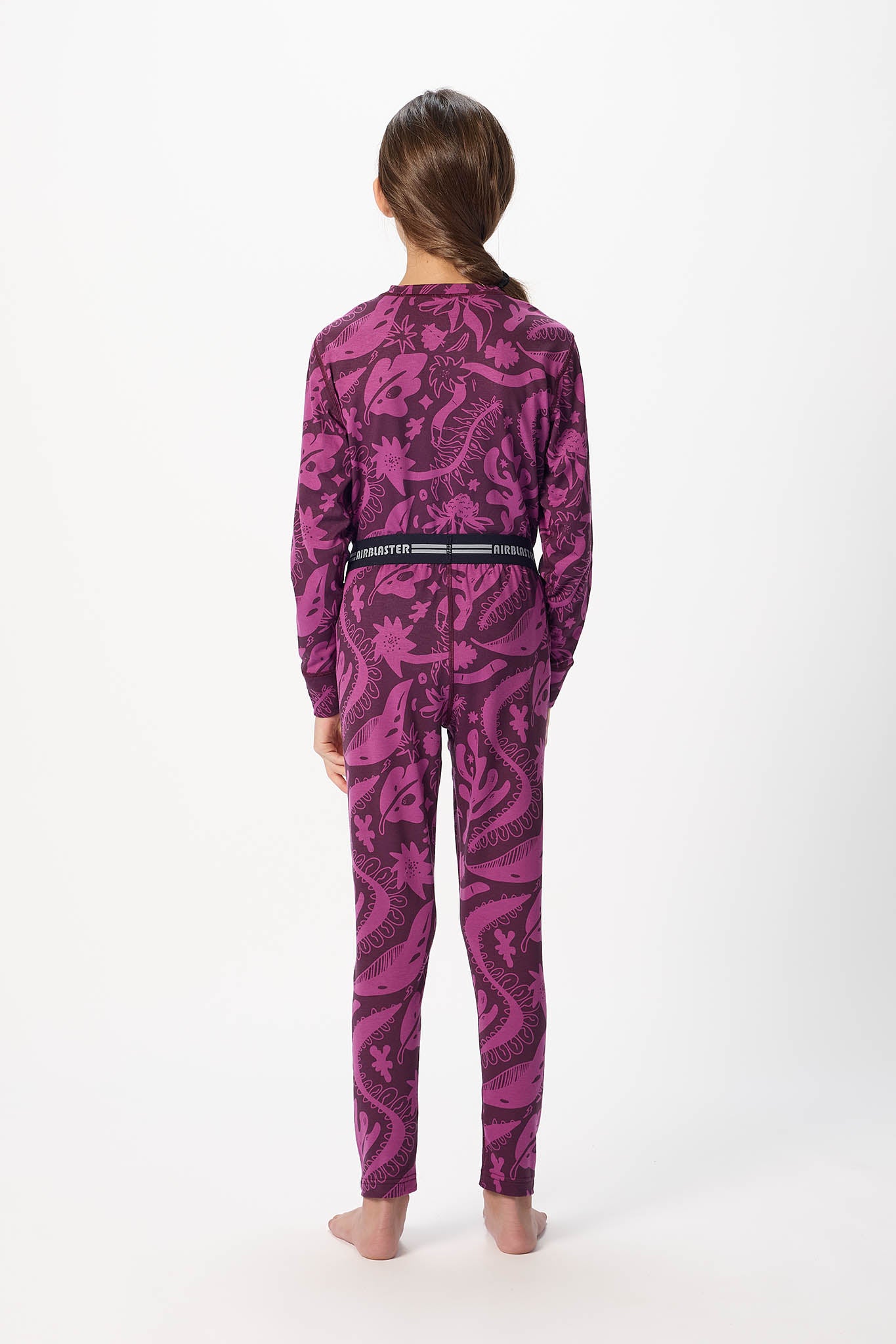 Youth model wearing Plum Earth life base layer bottoms, standing with back facing the camera with white background.