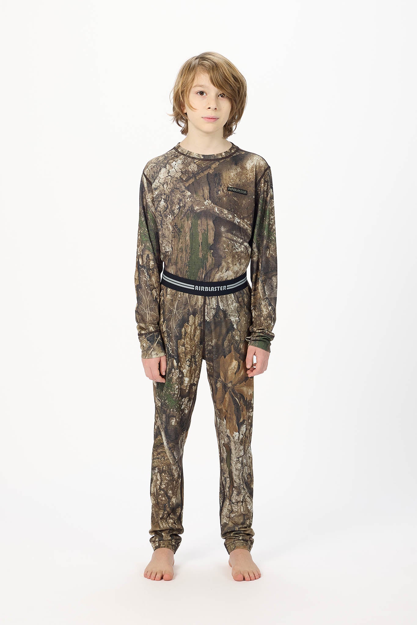 Youth standing center frame, wearing youth base RealTree Camouflage layer bottoms with white background.