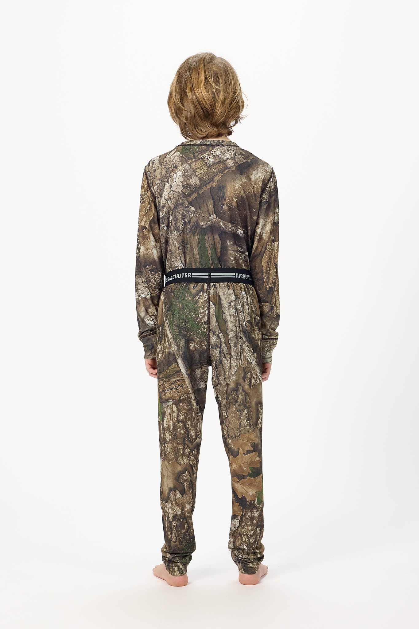 Youth model wearing RealTree Camouflage base layer bottoms,standing with his back facing the camera with a white background.