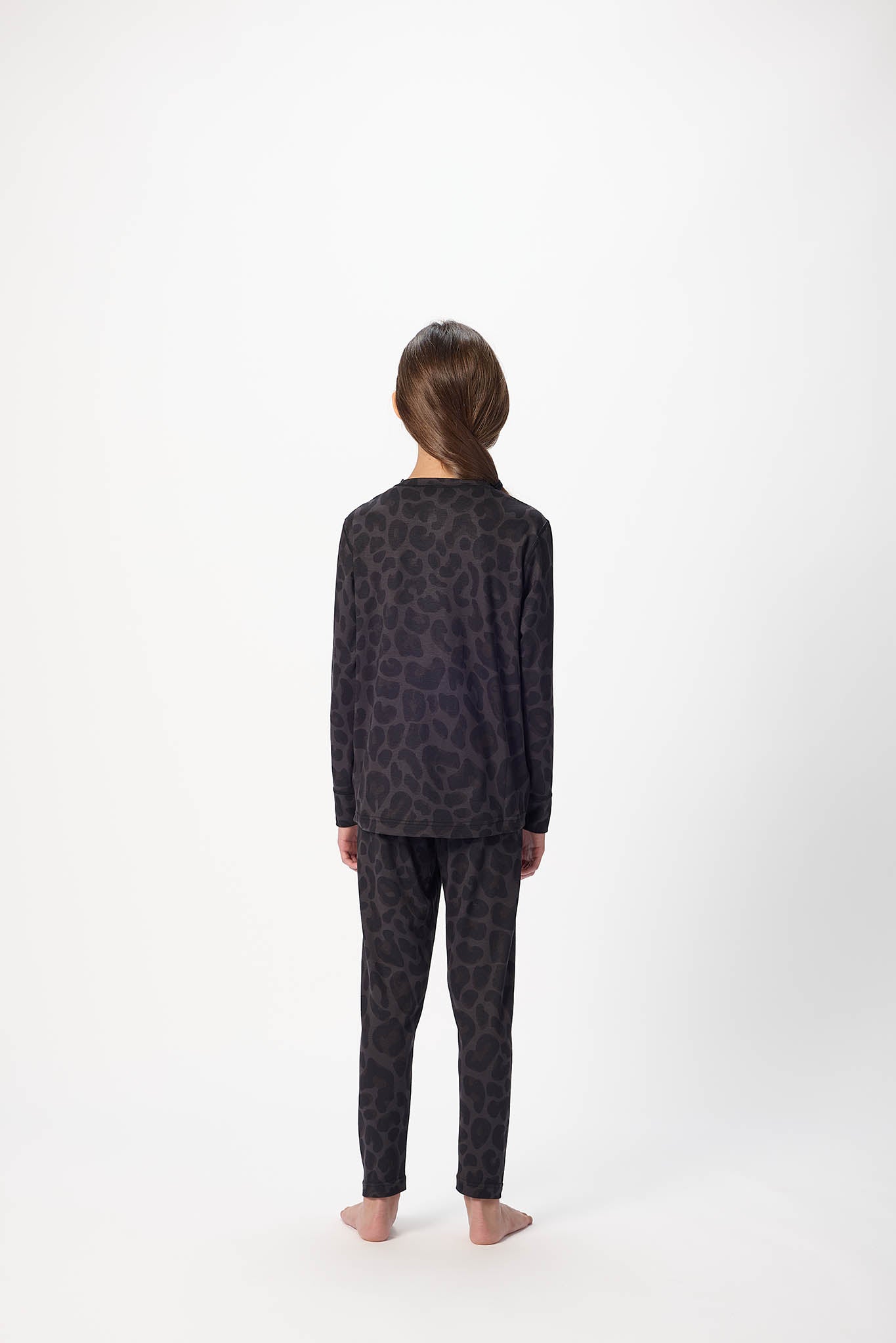 A child standing with their back to the camera, wearing a matching two-piece pajama set with a dark gray and black animal print pattern, photographed against a plain white studio background.