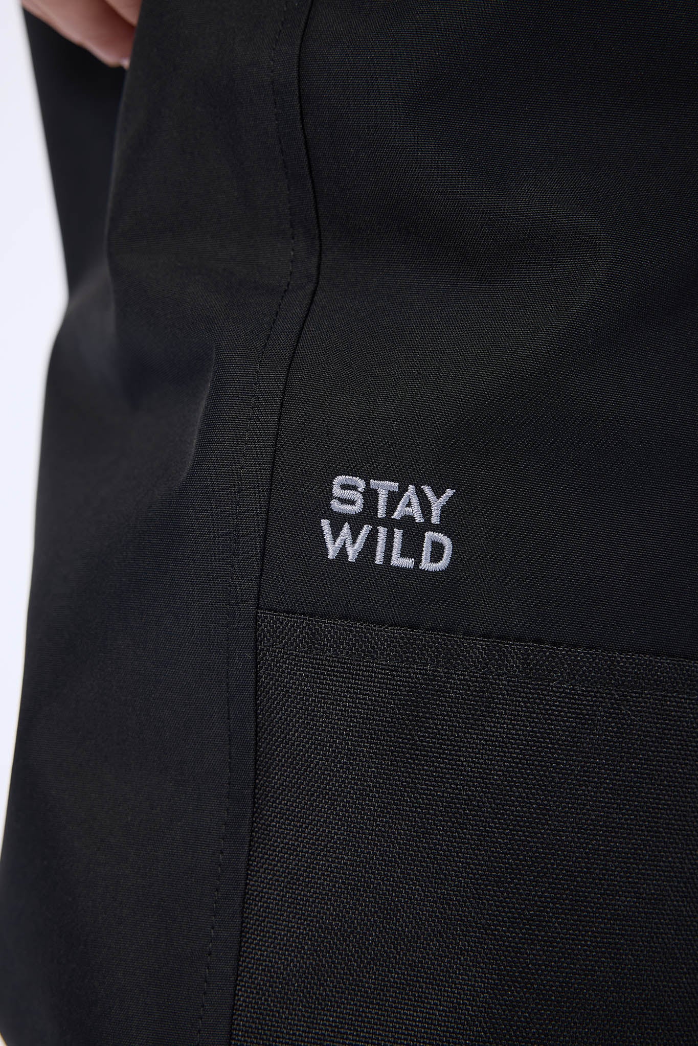 Close-up of a black garment with a small white embroidered logo reading 'STAY WILD' on the chest.