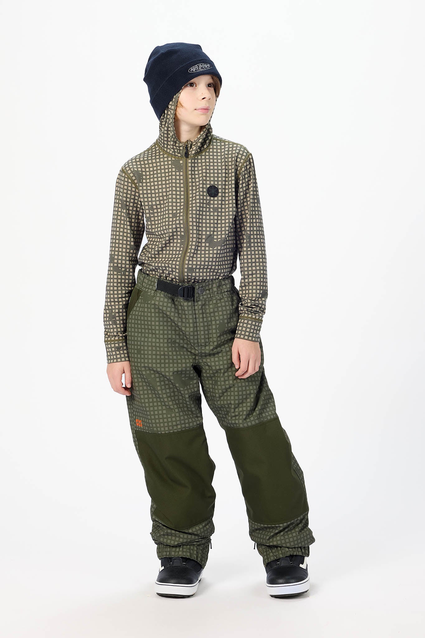 A child model wearing a matching two-piece outdoor jacket and pants set in an olive green and black micro-check pattern, paired with a black beanie and black sneakers, on a white studio background.