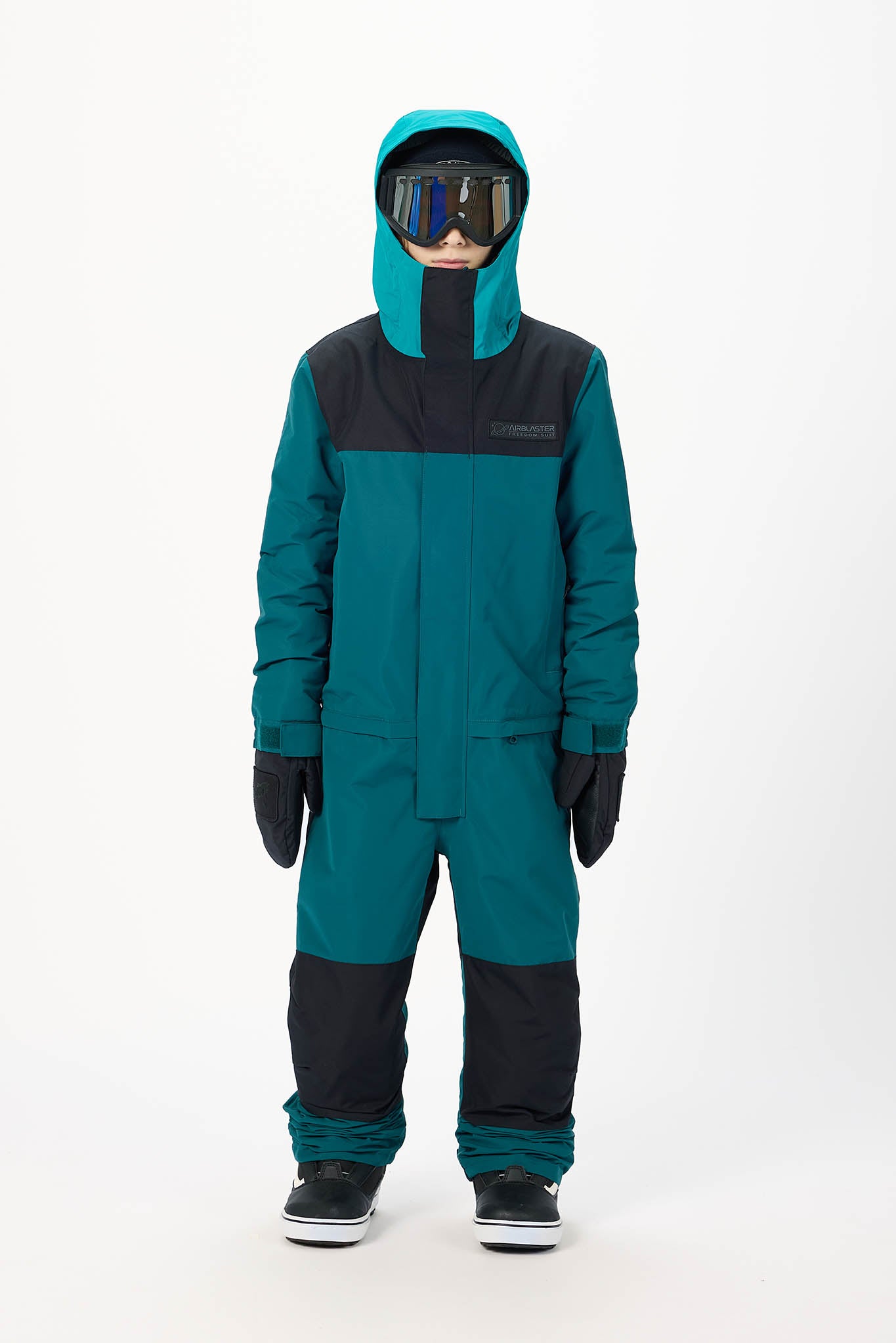 A child wearing a teal and black one-piece snowsuit with a hood, black gloves, and snow goggles, standing against a plain white studio background.