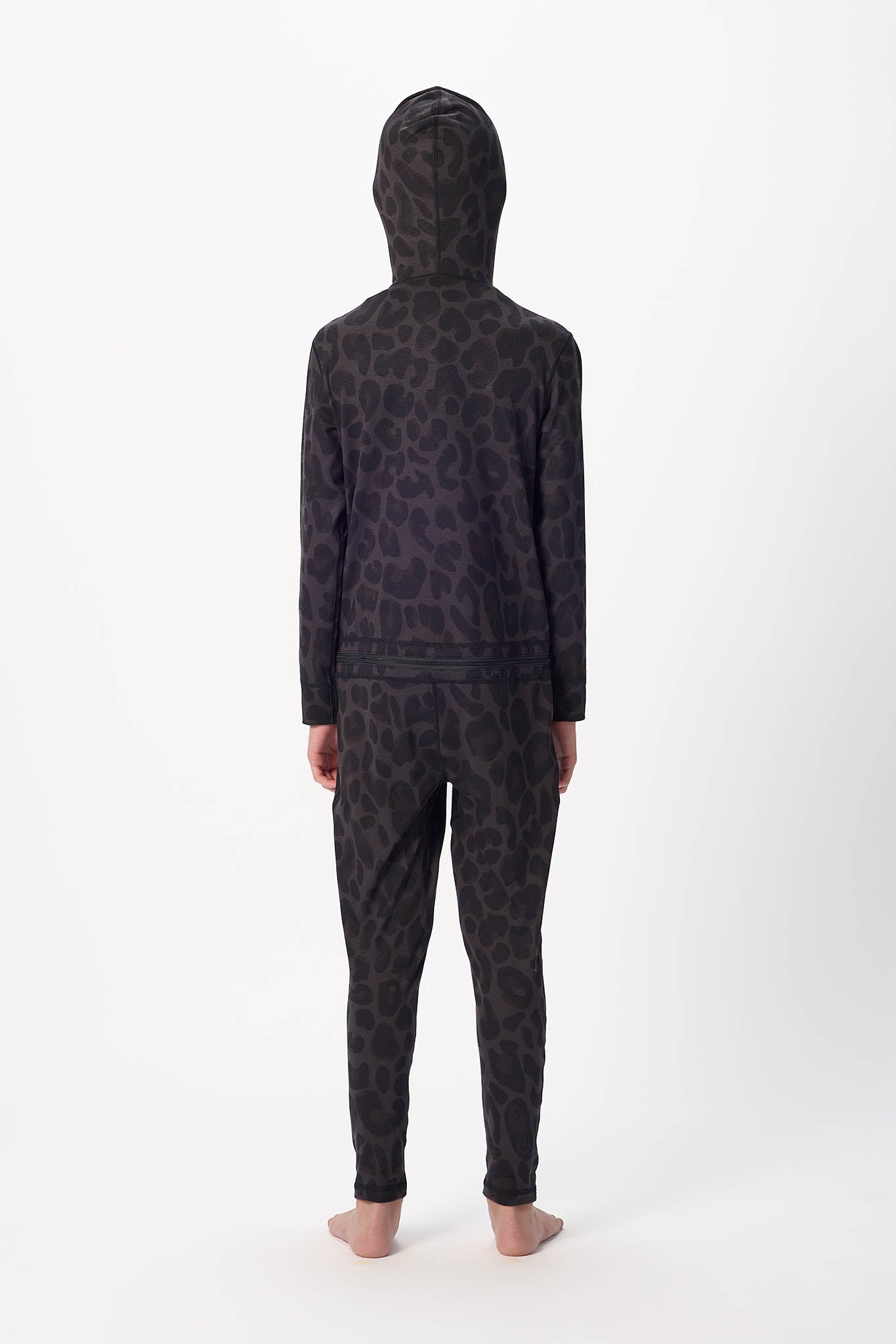 A child standing with their back to the camera, wearing a dark leopard-print hooded sweatshirt and matching pants against a plain white studio background.