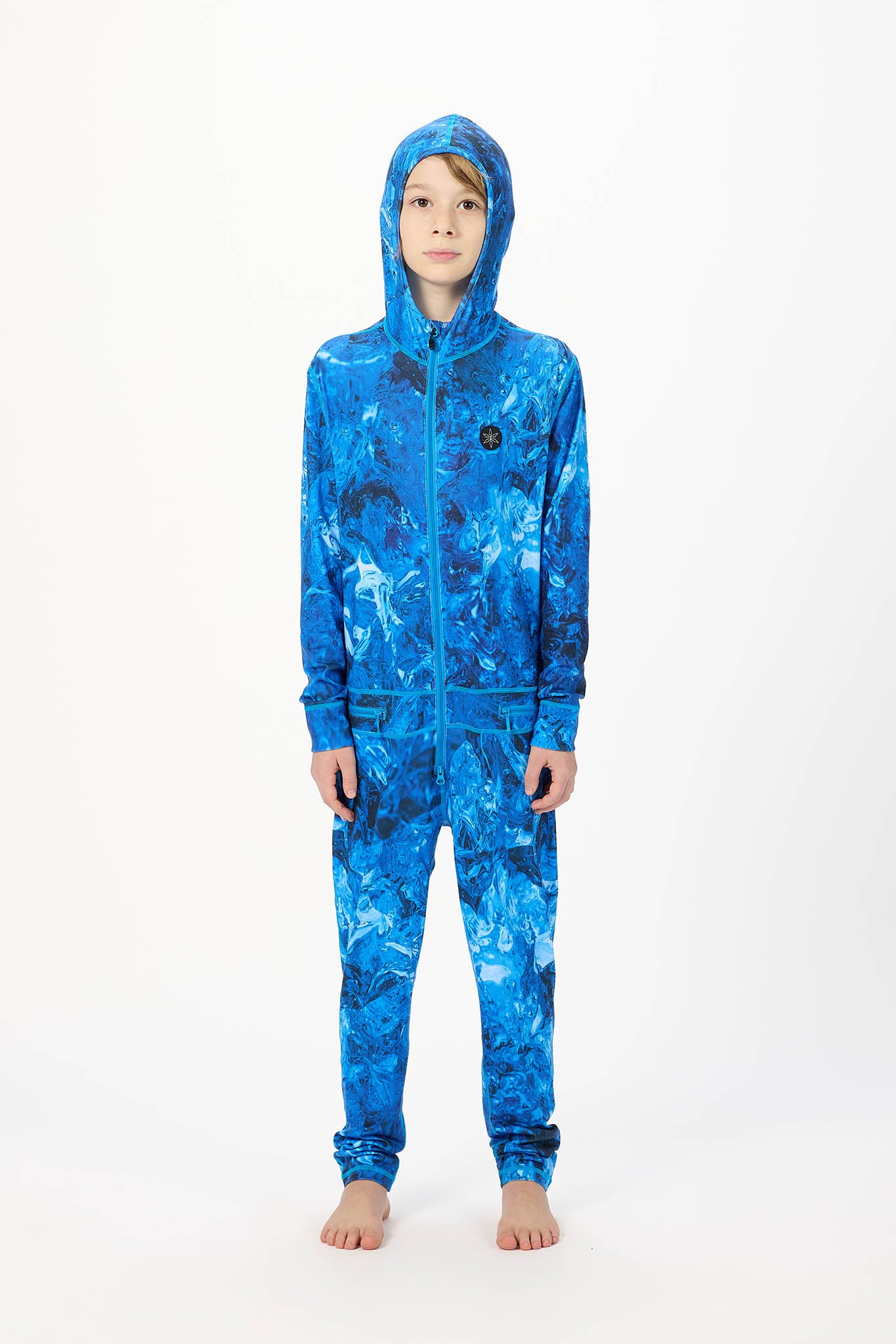 A child wearing a full-body hooded one-piece jumpsuit with an abstract blue and black marbled pattern, standing against a plain white studio background.