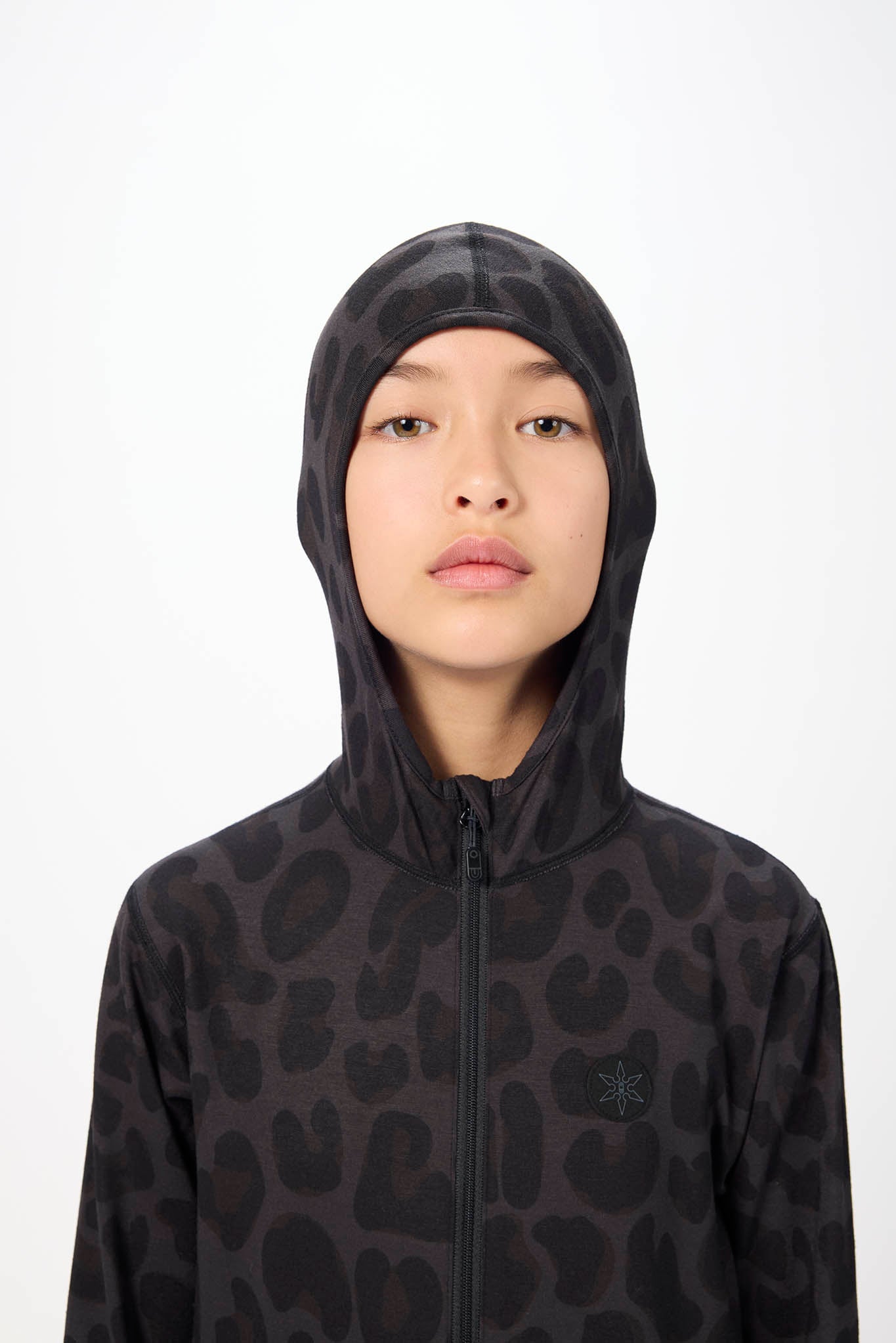 A model wearing a black hooded zip-up jacket with a dark gray abstract animal print pattern, featuring a small tonal star logo on the left chest, set against a plain white background.