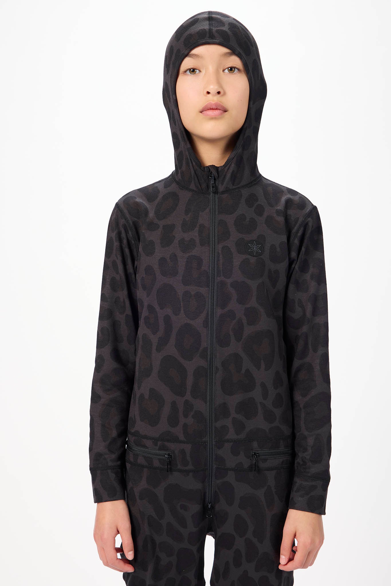 A model wearing a black hooded zip-up jacket with a dark gray animal spot pattern, photographed against a plain white studio background.