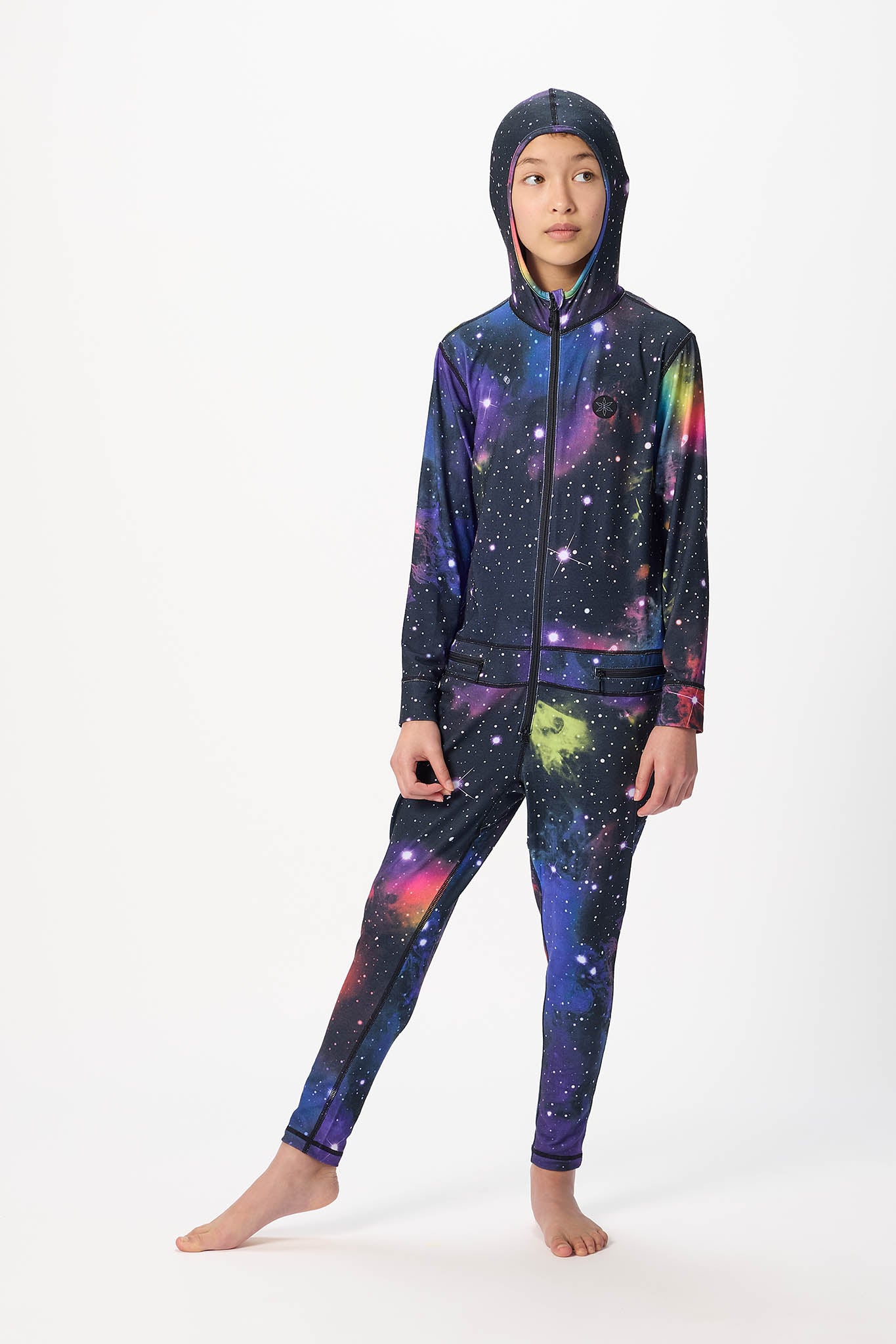 A child model wearing a full-body hooded tracksuit with a colorful galaxy print, standing against a plain white studio background.