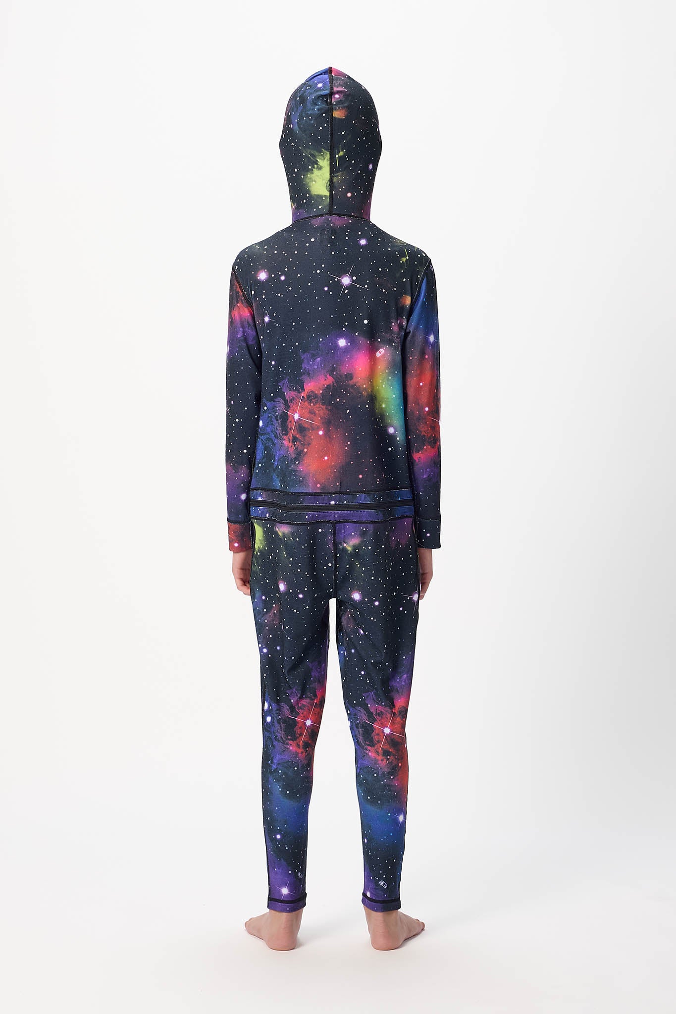 A child standing with their back to the camera, wearing a matching hooded sweatshirt and jogger pants set with a vibrant galaxy print on a white studio background.