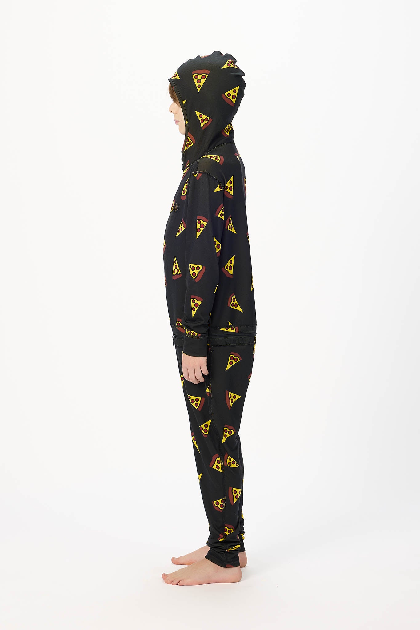 A child standing in profile wearing a black hooded sweatshirt and matching pants with an allover yellow pizza slice print, photographed against a plain white studio background.